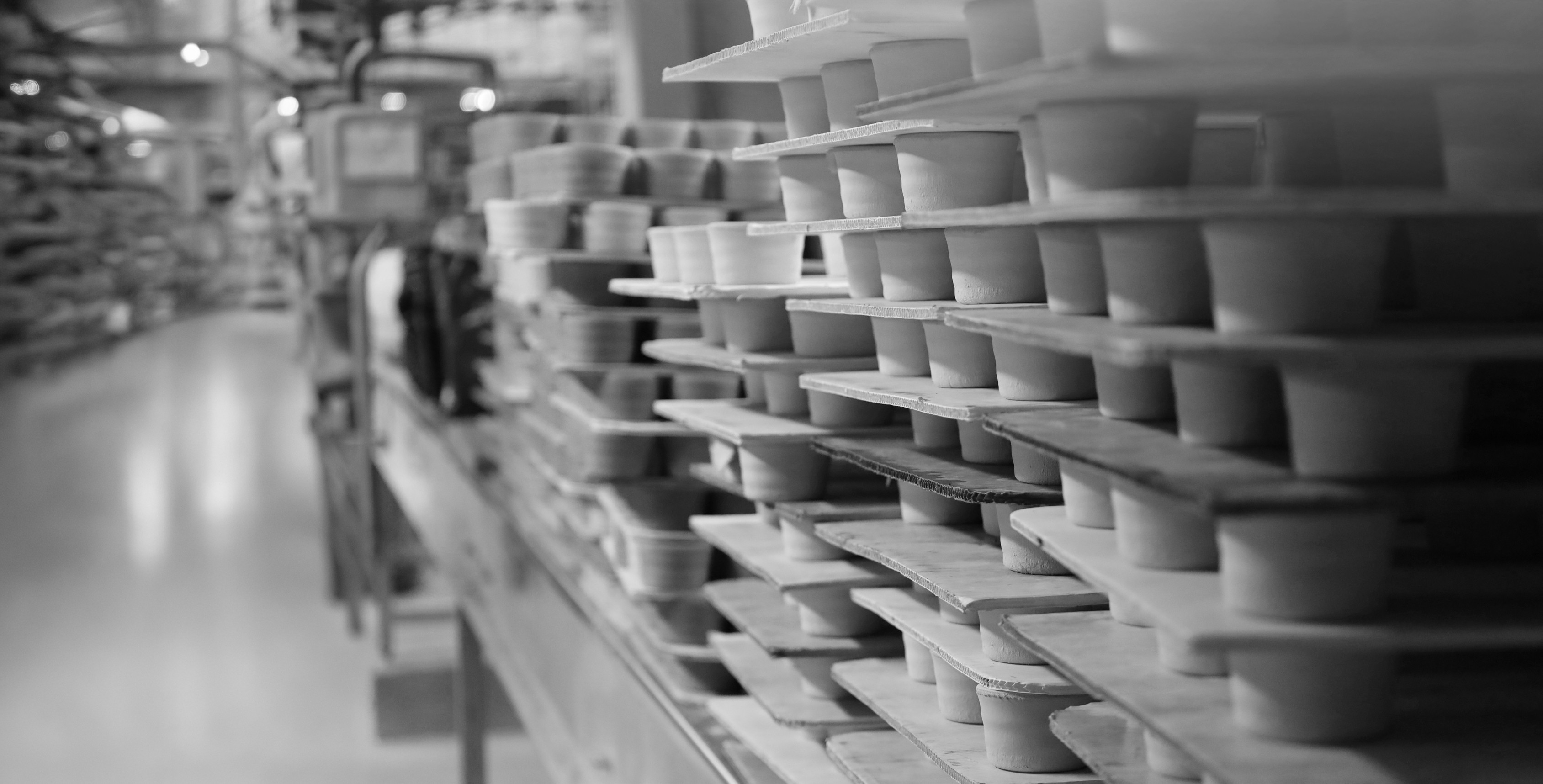 Rangées de pièces en céramique crue posées sur des planches en bois dans un atelier de fabrication, photographie en noir et blanc
