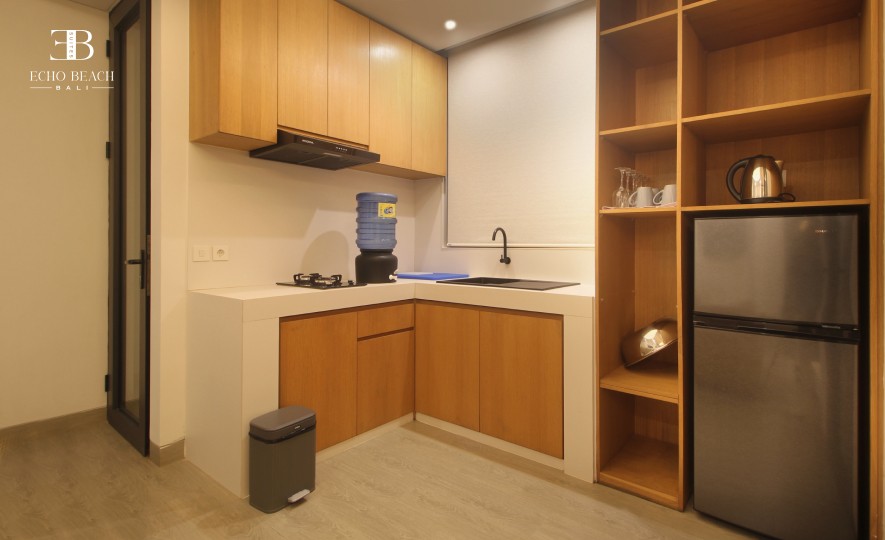 Compact and functional kitchen space with modern wooden cabinets, fridge, and stovetop in the three bathroom Echo Beach Suite apartment, Bali.