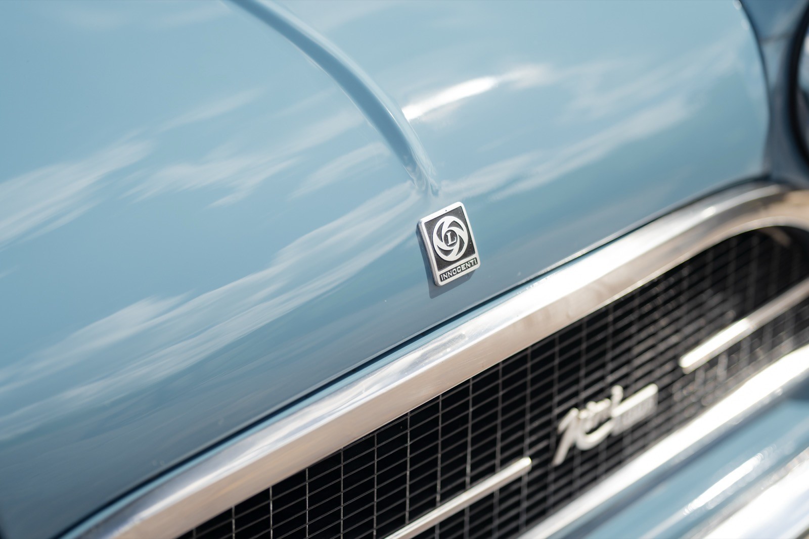 Close-up of a vintage blue car's hood and grille, featuring chrome accents and smooth paint texture.