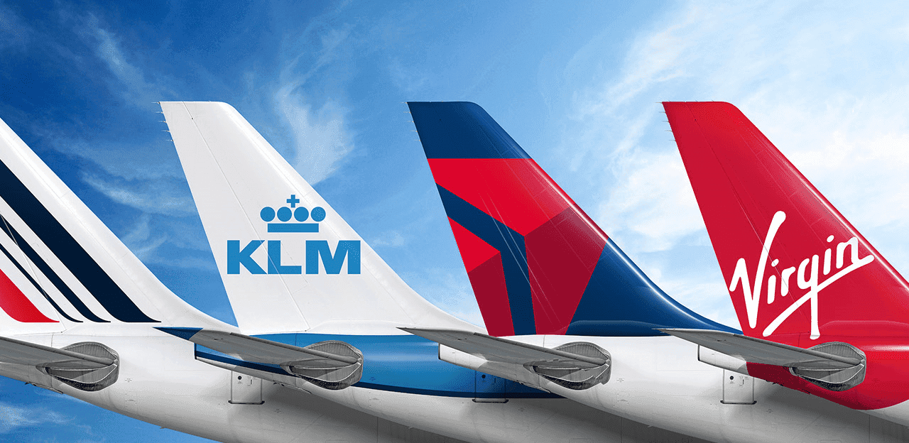 Close-up of two smiling friends with freckles, bright makeup, on a light blue background—joyful, inclusive brand portrait.