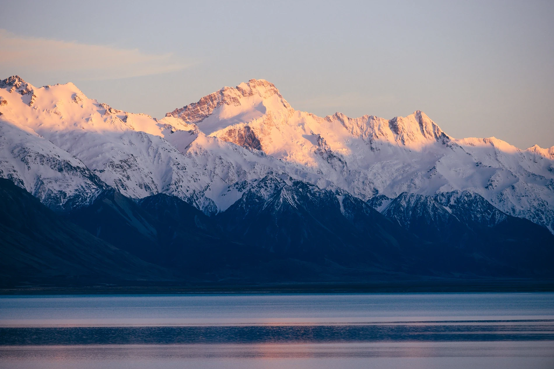 Alpine glow on a snow-covered peak above a still lake at dusk