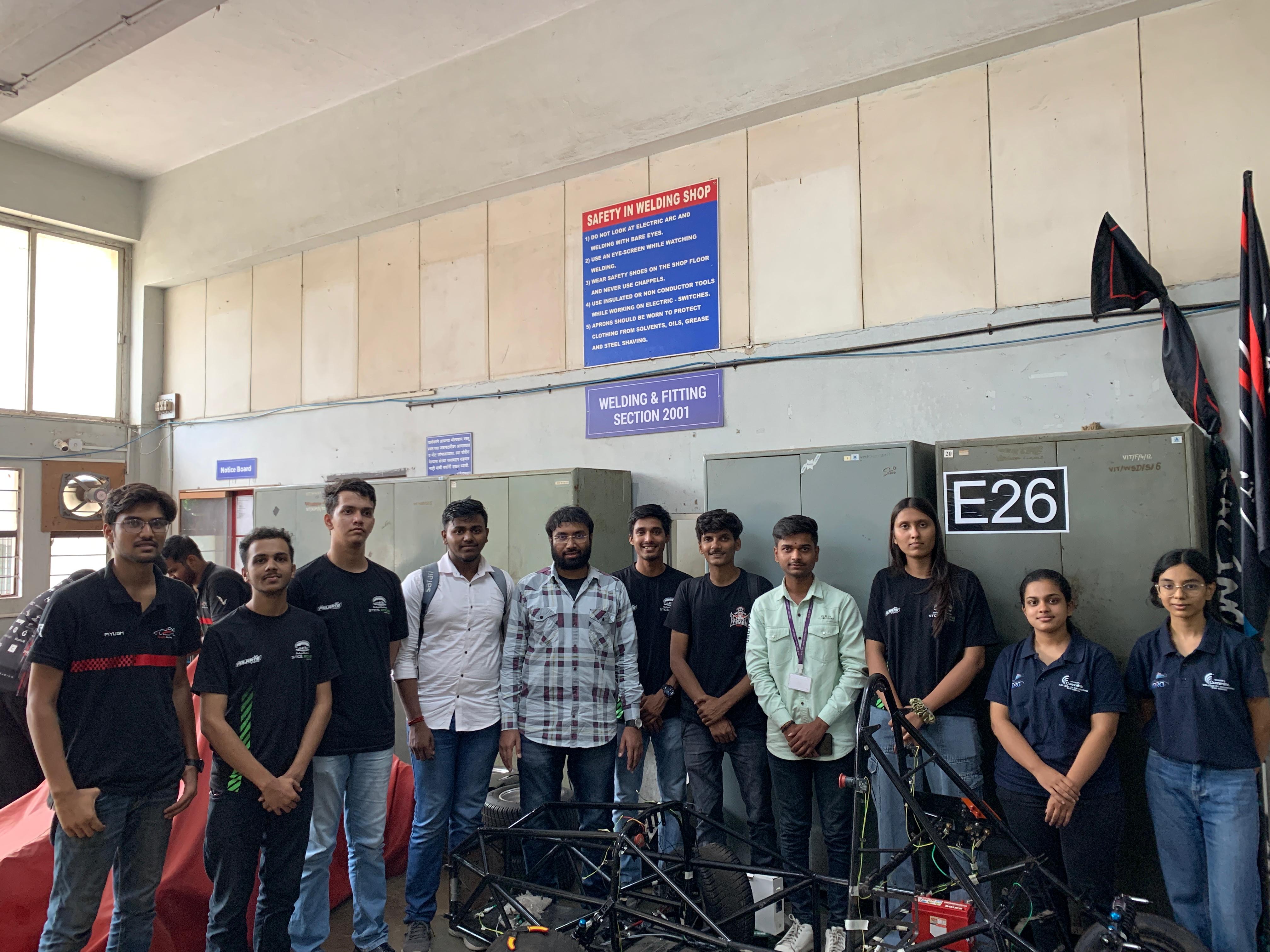 A woman with wavy hair sits at a desk, focused on writing, surrounded by colorful art and plants.