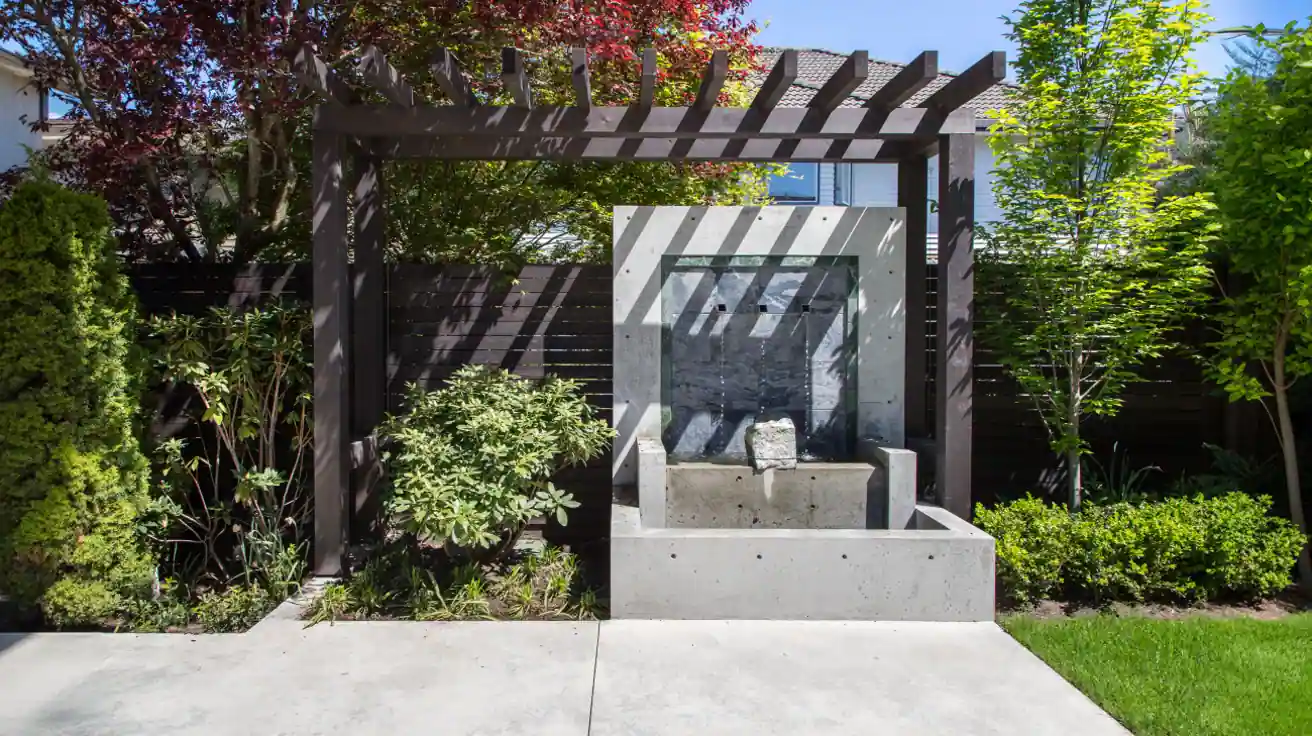 Architectural outdoor water feature with modern pergola, tiered concrete design, professional landscaping, and decorative Japanese maple tree