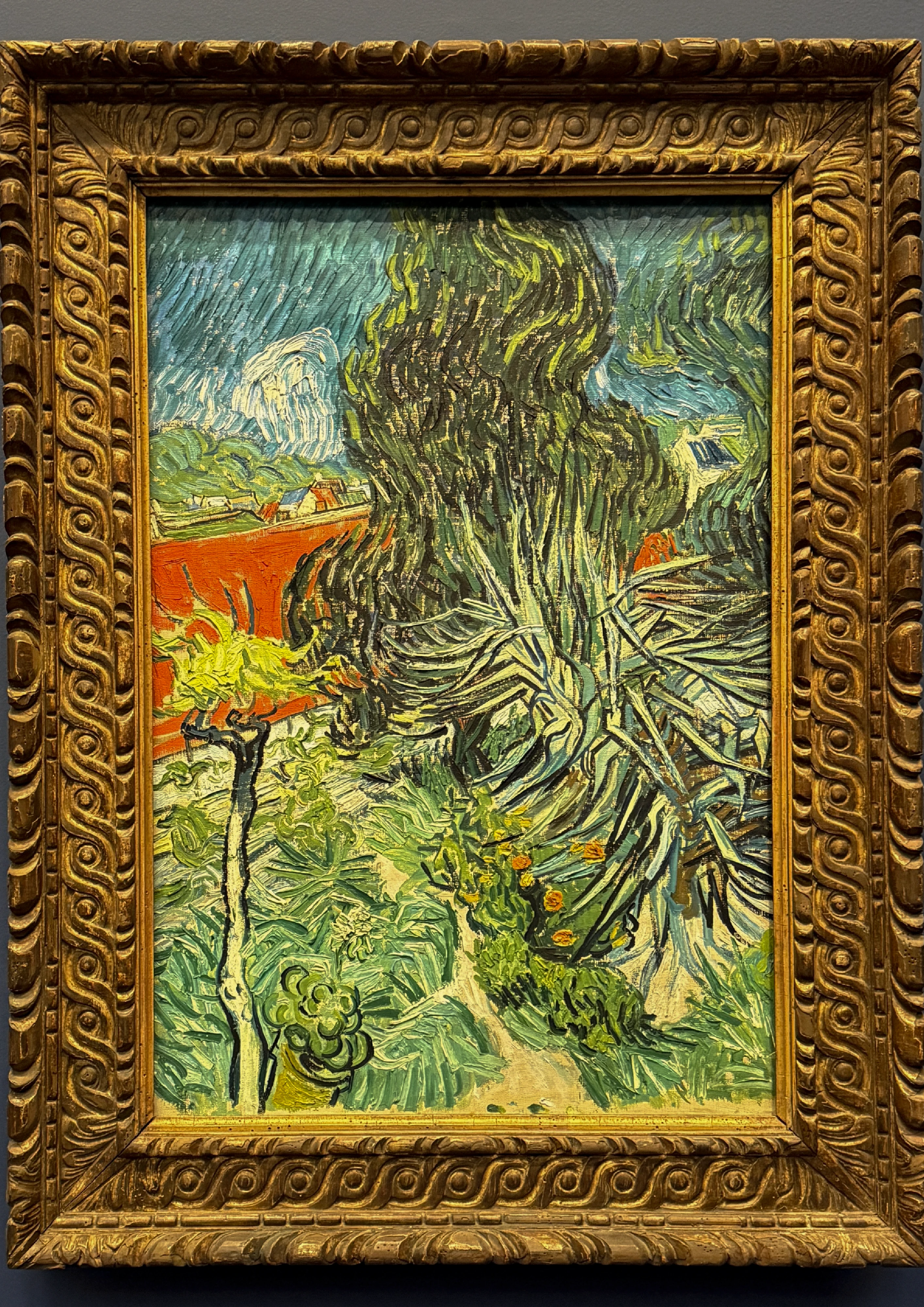 Painting of a dense garden in thick, restless brushstrokes, almost entirely green foliage with a patch of red wall behind.