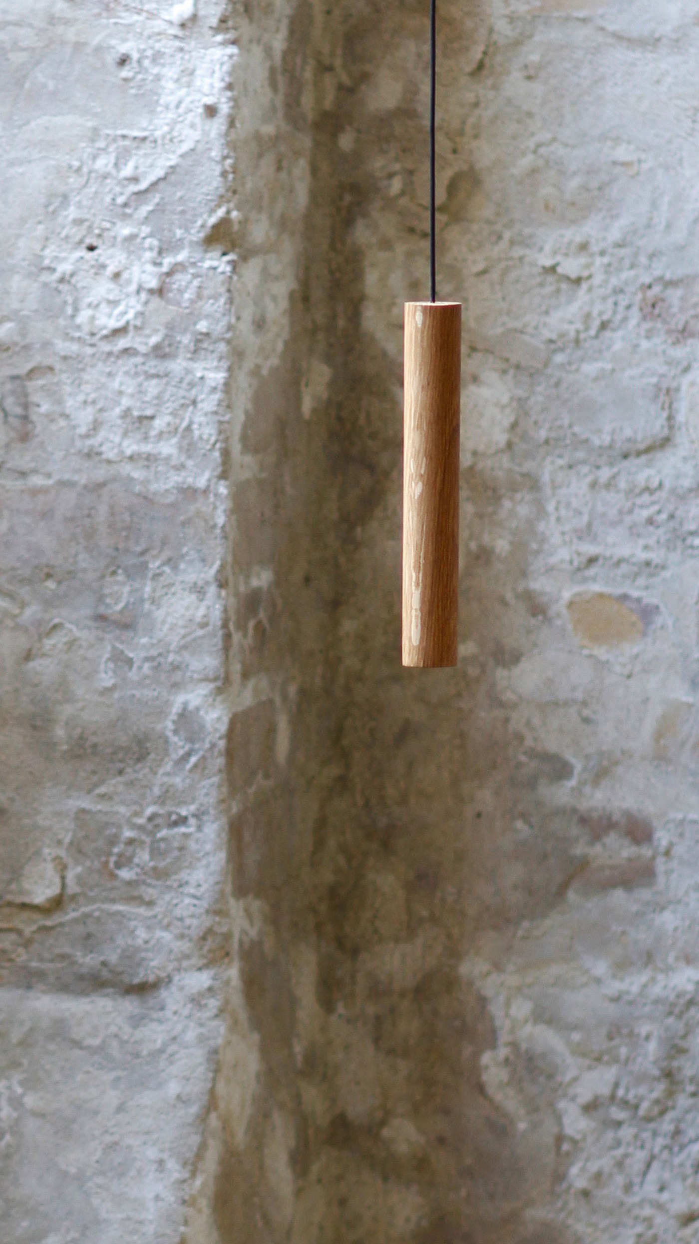 Chimes pendant lamp in solid oak suspended against textured brick wall designed by Asger Risborg Jakobsen