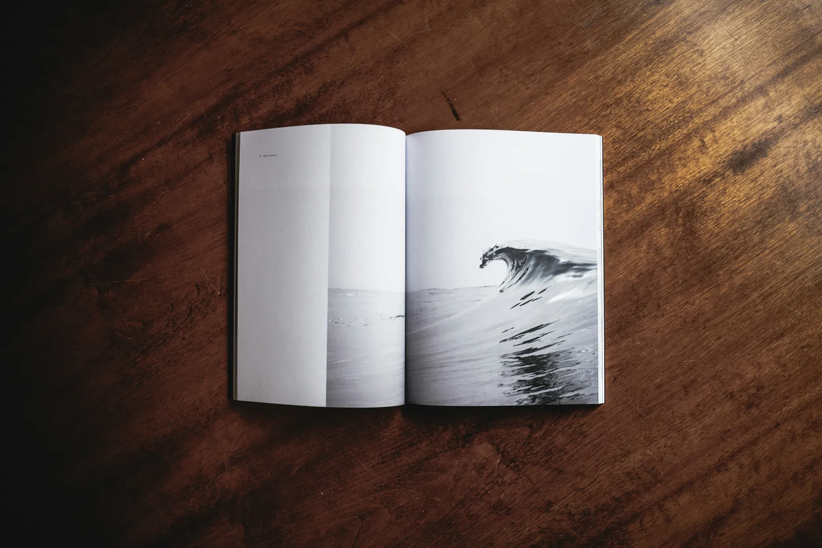 An open magazine on a wooden table, showing a black and white photograph of a breaking wave