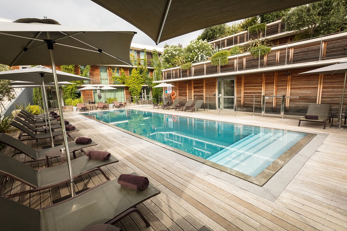 A pool surrounded by lounge chairs and umbrellas, located in Courtyard by Marriott in front of a building.