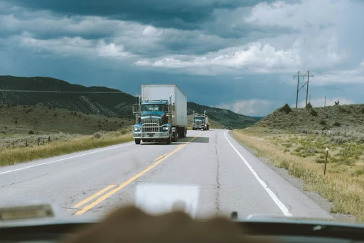 Semi-trucks driving on a rural highway under cloudy skies, viewed from a vehicle