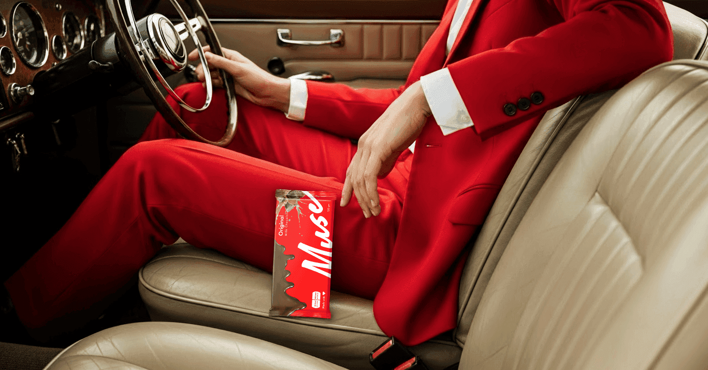 Person in a red suit sitting in a vintage car, holding a Muse cosmetic product black and white image 