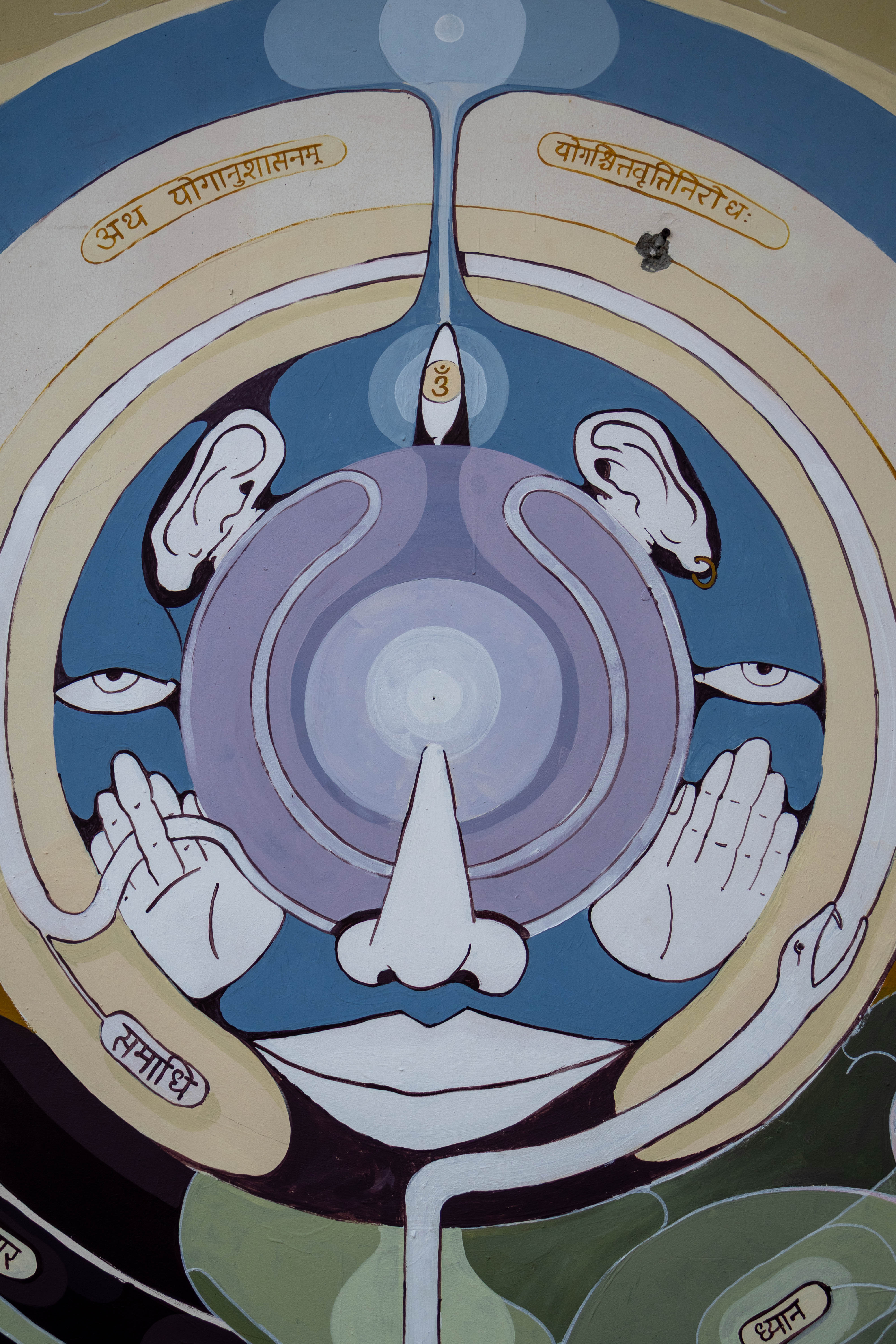 Abstract painting with stylized facial features, hands, ears, eyes, and Sanskrit script arranged in symmetrical, circular patterns, using shades of blue, beige, and purple.