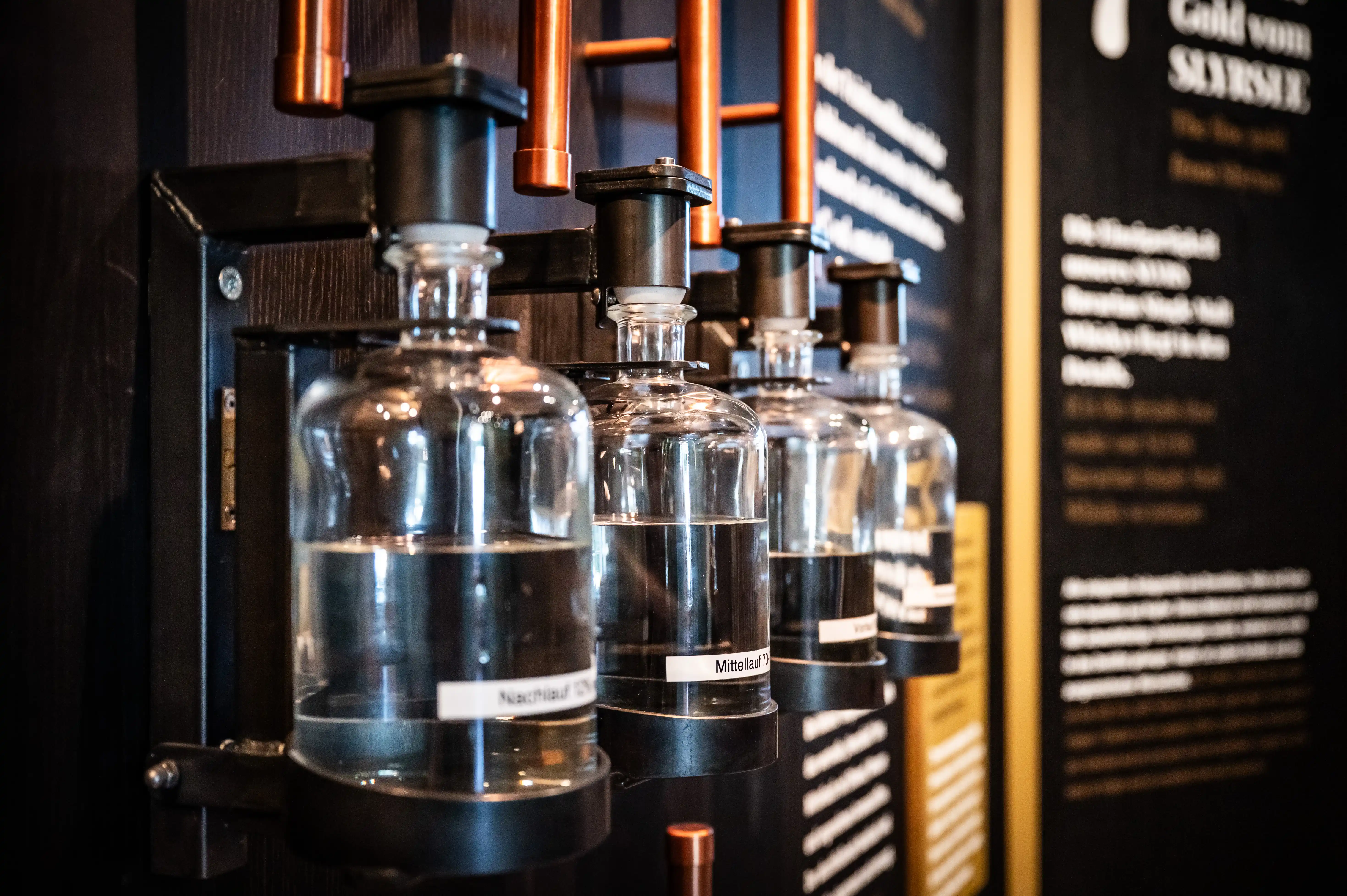 Scent station with glass flasks and copper pipes on a dark exhibition wall at the SLYRS whisky experience.