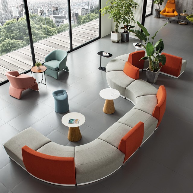 Modern modular curved sectional sofa in a gray and orange palette within a bright, open-concept office lounge overlooking a city skyline.