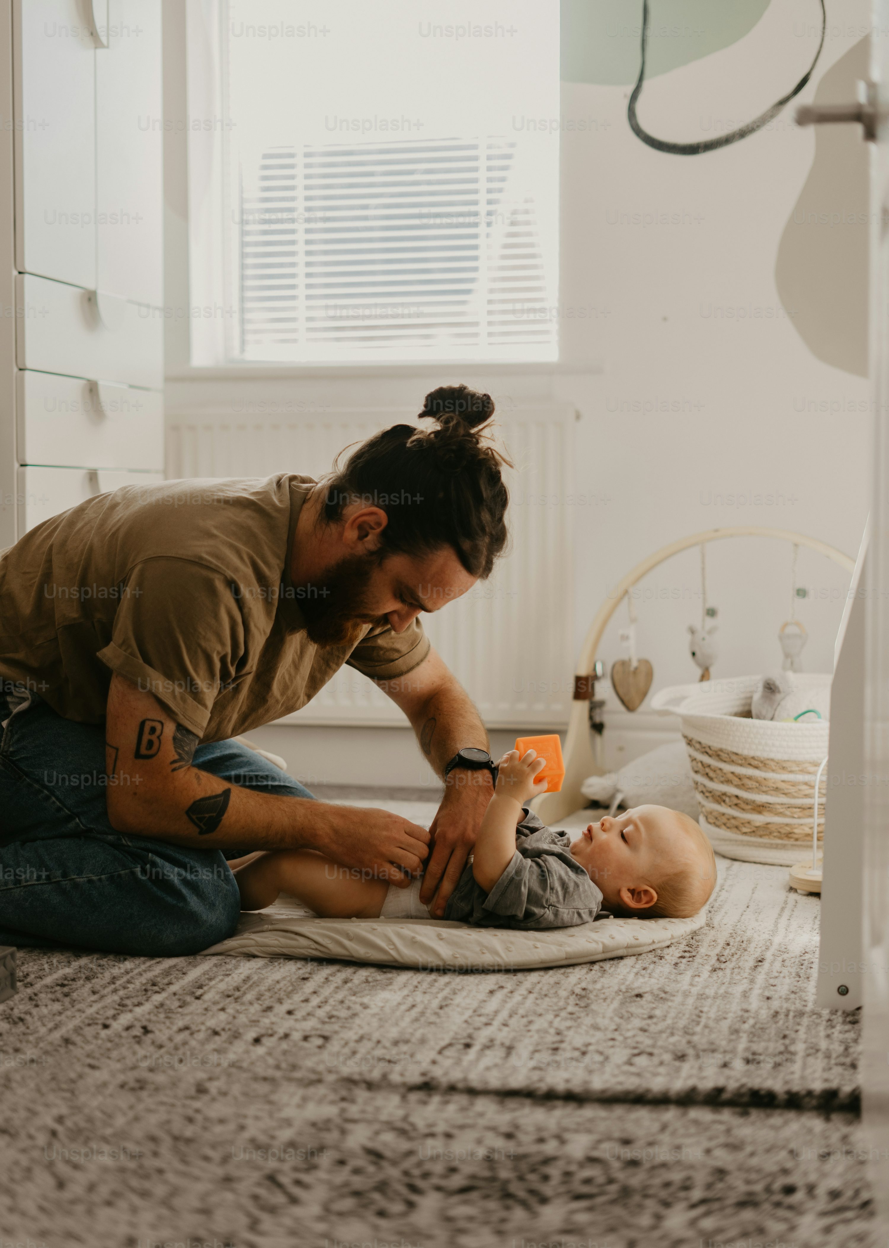 A father on the floor playing with his baby, modeling the engaged parent interaction that supports early development.