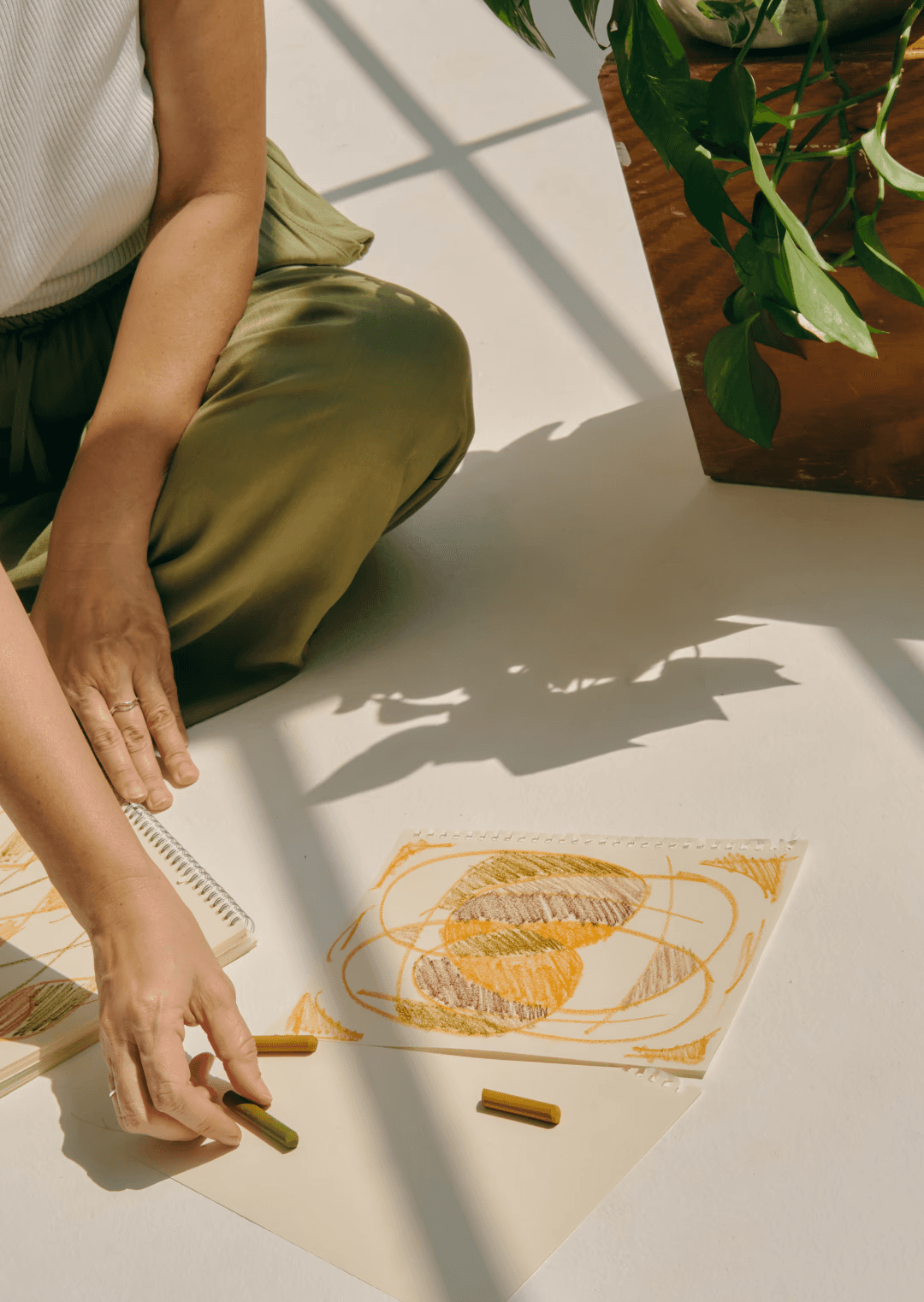 Girl sitting on the floor, drawing with orange and brown crayons on white paper, symbolizing the importance of mindfulness in mental and emotional wellbeing.