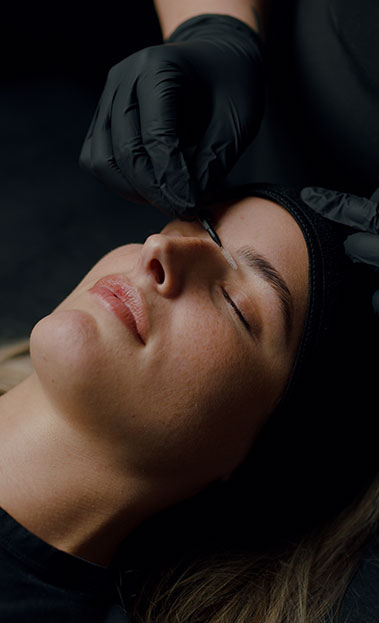 Close-up portrait of a person wearing a gray insulated hooded jacket with the hood up, showing their face framed by the hood against a light background.