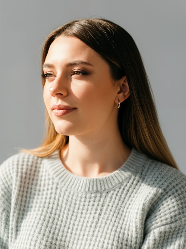 A woman with straight blonde hair wearing a light colored sweater looks away.