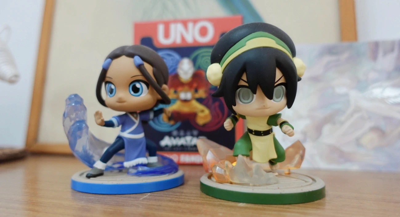 Katara and Toph collectible figurines standing in front of an Avatar-themed Uno card game.