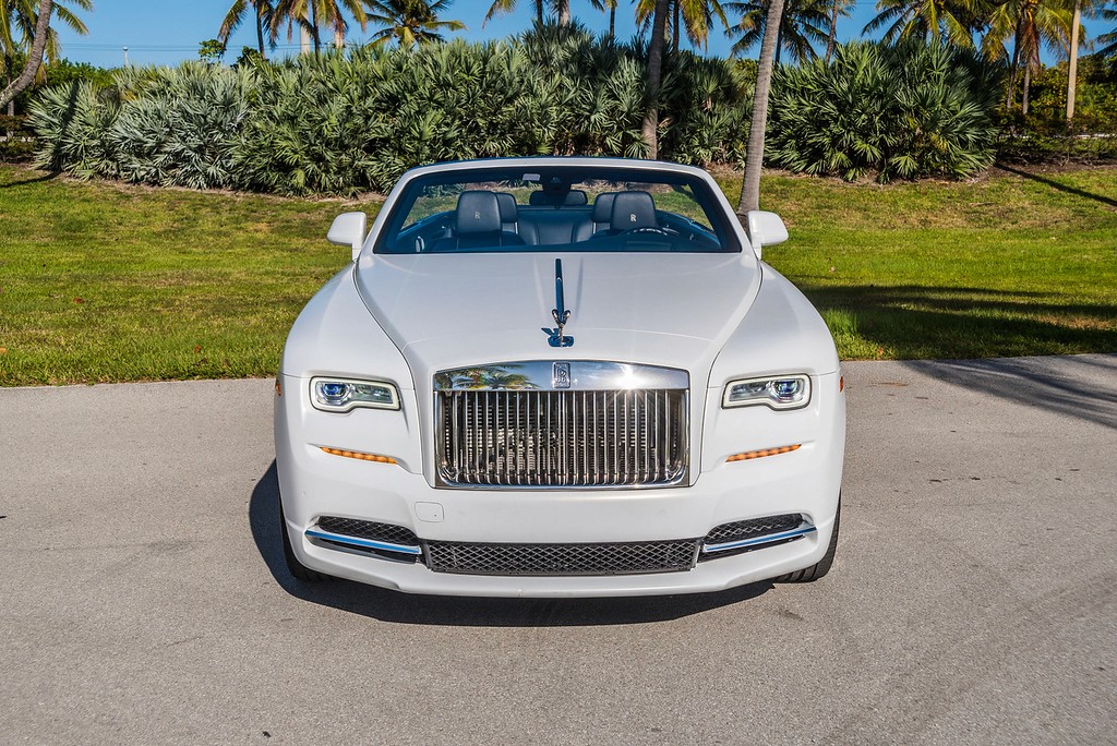 Close-up of the Rolls-Royce Dawn’s front grille and Spirit of Ecstasy emblem, with a scenic backdrop of palm trees and clear skies.