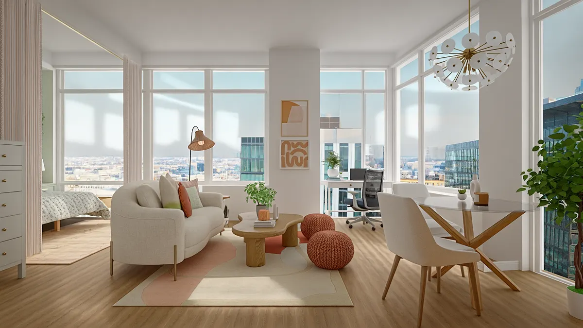 Wide view of a bright studio apartment showing a living area, a dining set, and an office nook by floor-to-ceiling windows.