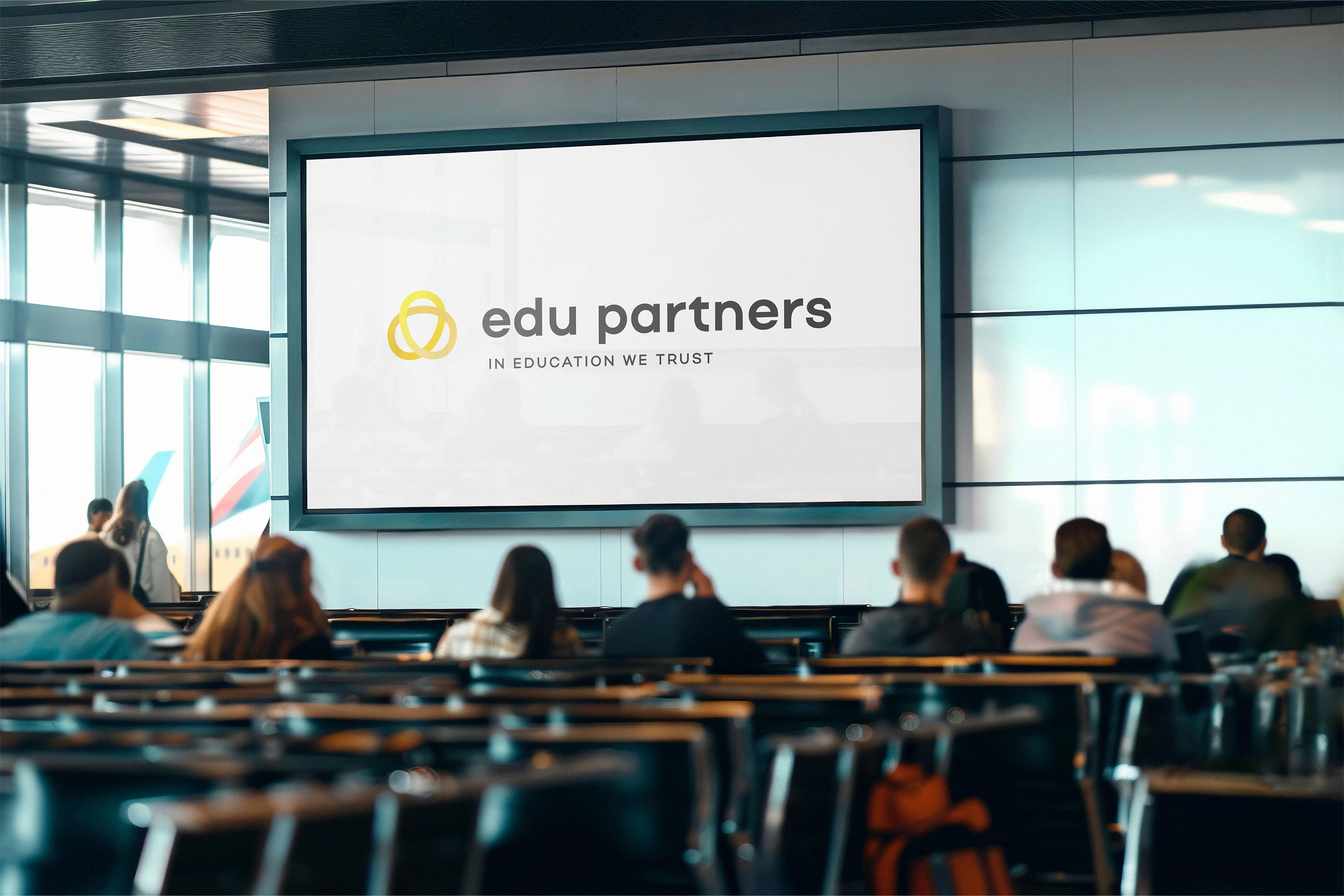 Logo Edu Partners zobrazené na velké obrazovce v konferenční hale s přítomnými lidmi.