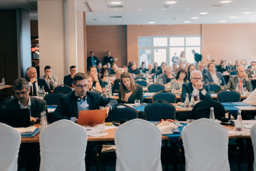 person discussing while standing in front of a large screen in front of people inside dim-lighted room