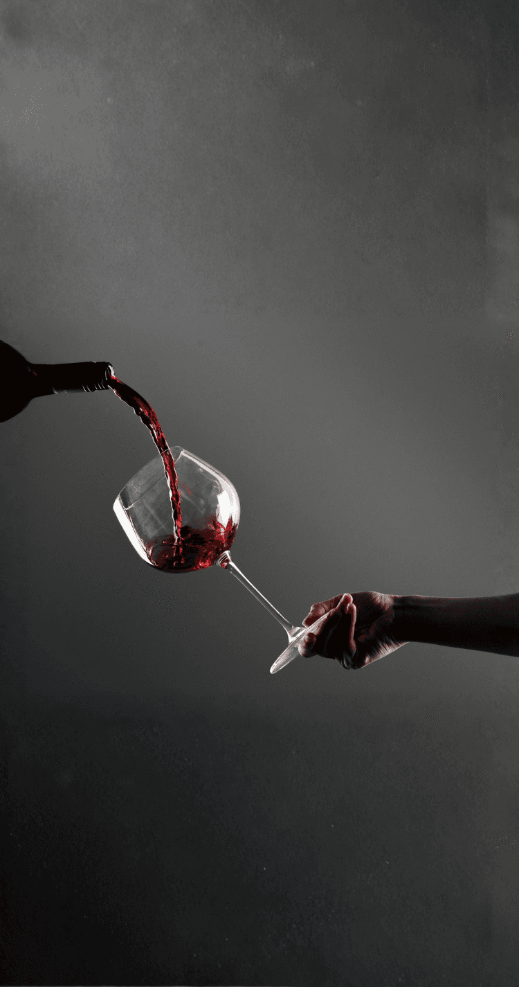 Photo d'un bras tenant un verre de vin dans lequel coule du rouge