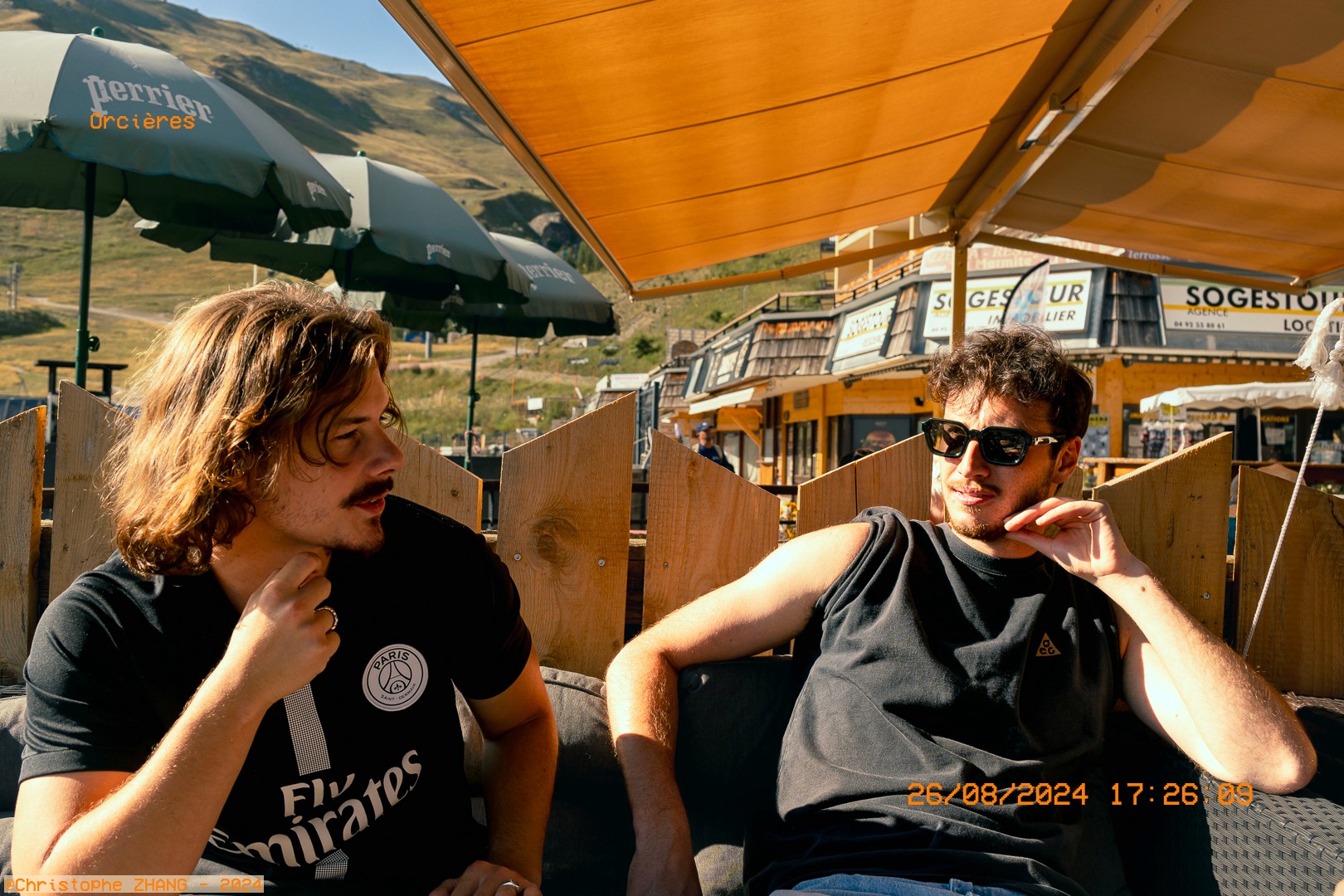 Deux amis discutent en terrasse à Orcières, sous le soleil de fin d’après-midi.
