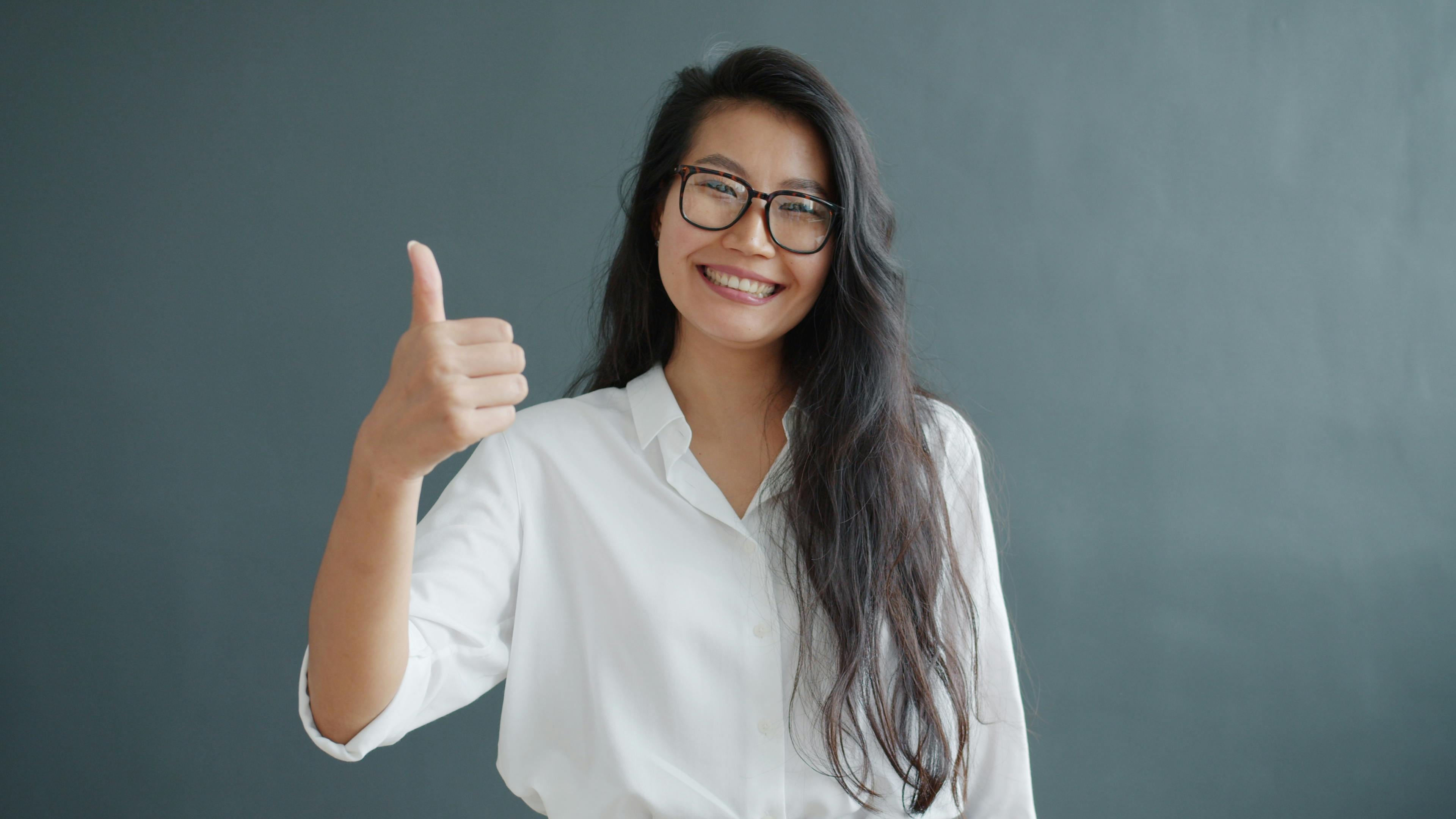 smiling-woman-in-glasses-and-white-shirt-giving-a-thumbs-up-against-gray-backgro - vitaly-gariev (pexels)