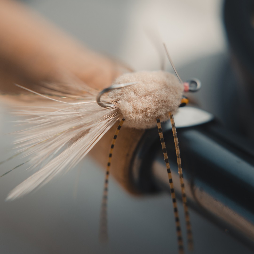 Closeup of a tan raghead permit fly on top of a fly rod handle