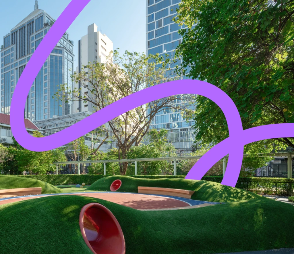 Colorful playground with green structures, a large clock, flowers, and city skyline in the background.