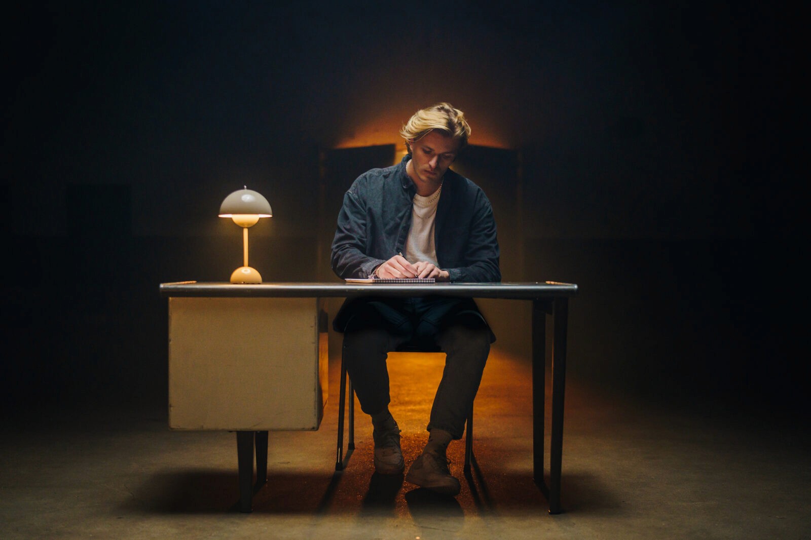 the image captures a guy sitting on a desk writing his goodbye letter to his parents