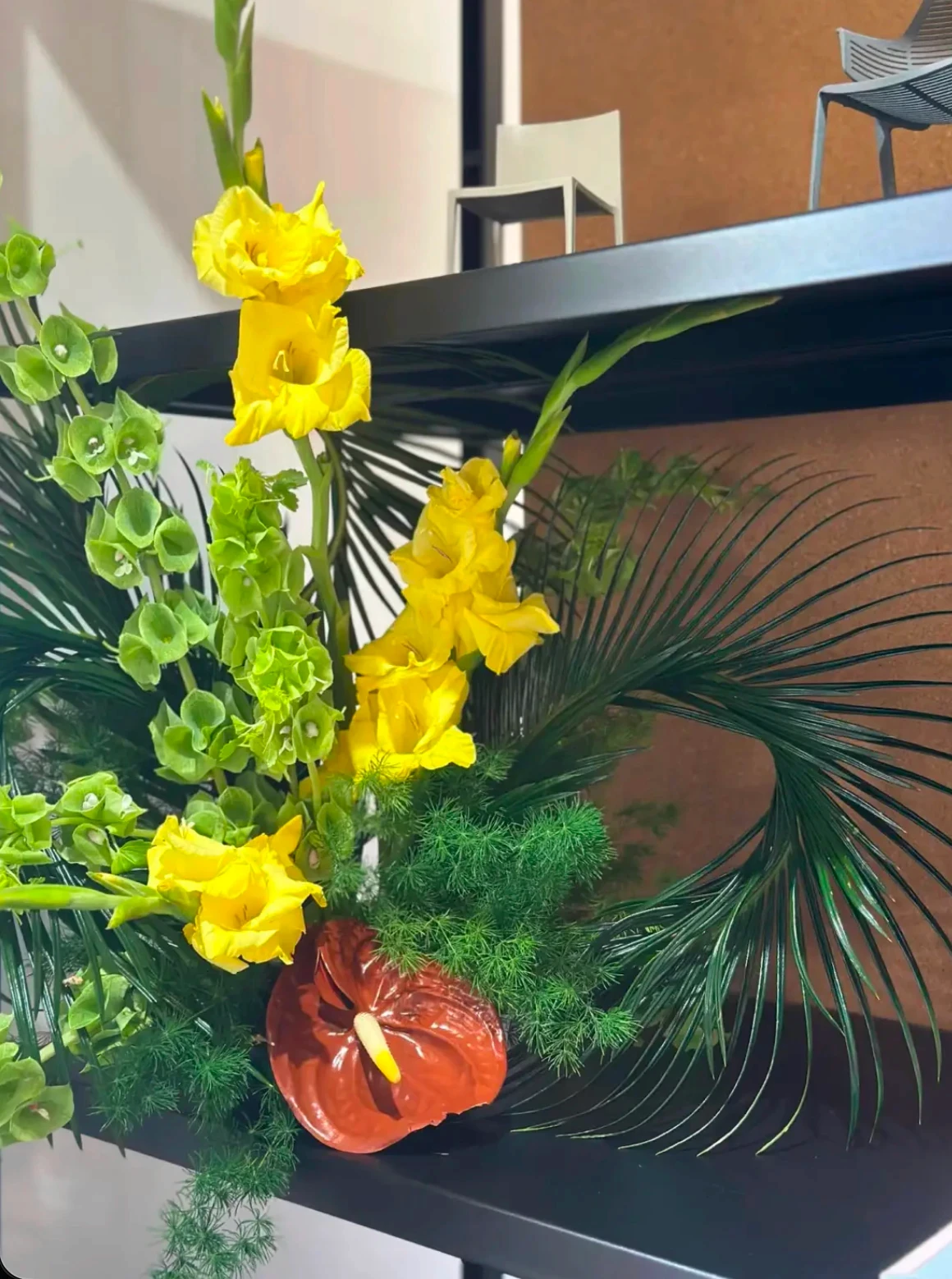 Primer plano de gladiolos amarillos y anturio marrón con líneas orgánicas y follaje tropical.