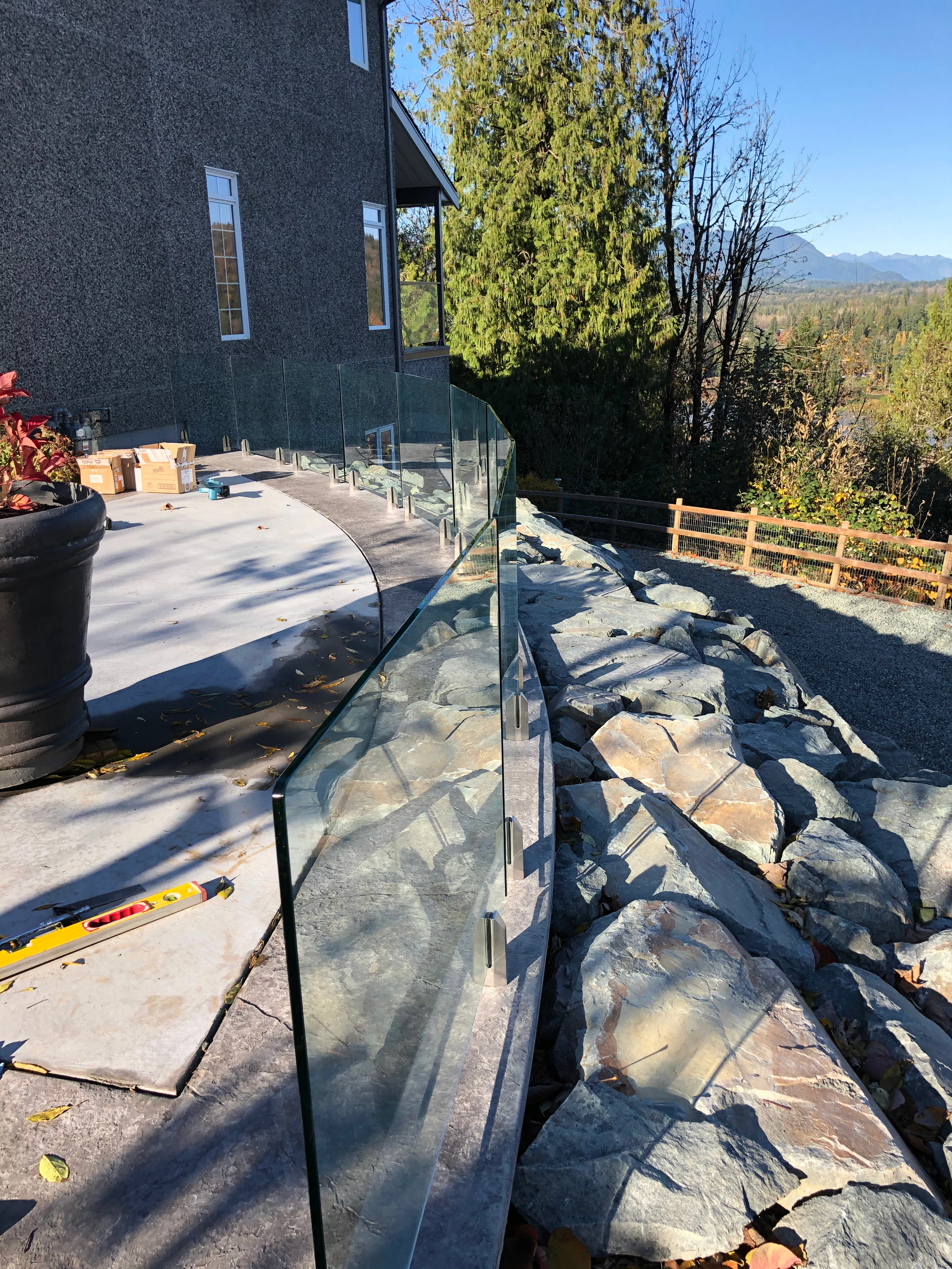 Topless glass railing with no cap rail running along a curved concrete patio edge above a stone retaining wall