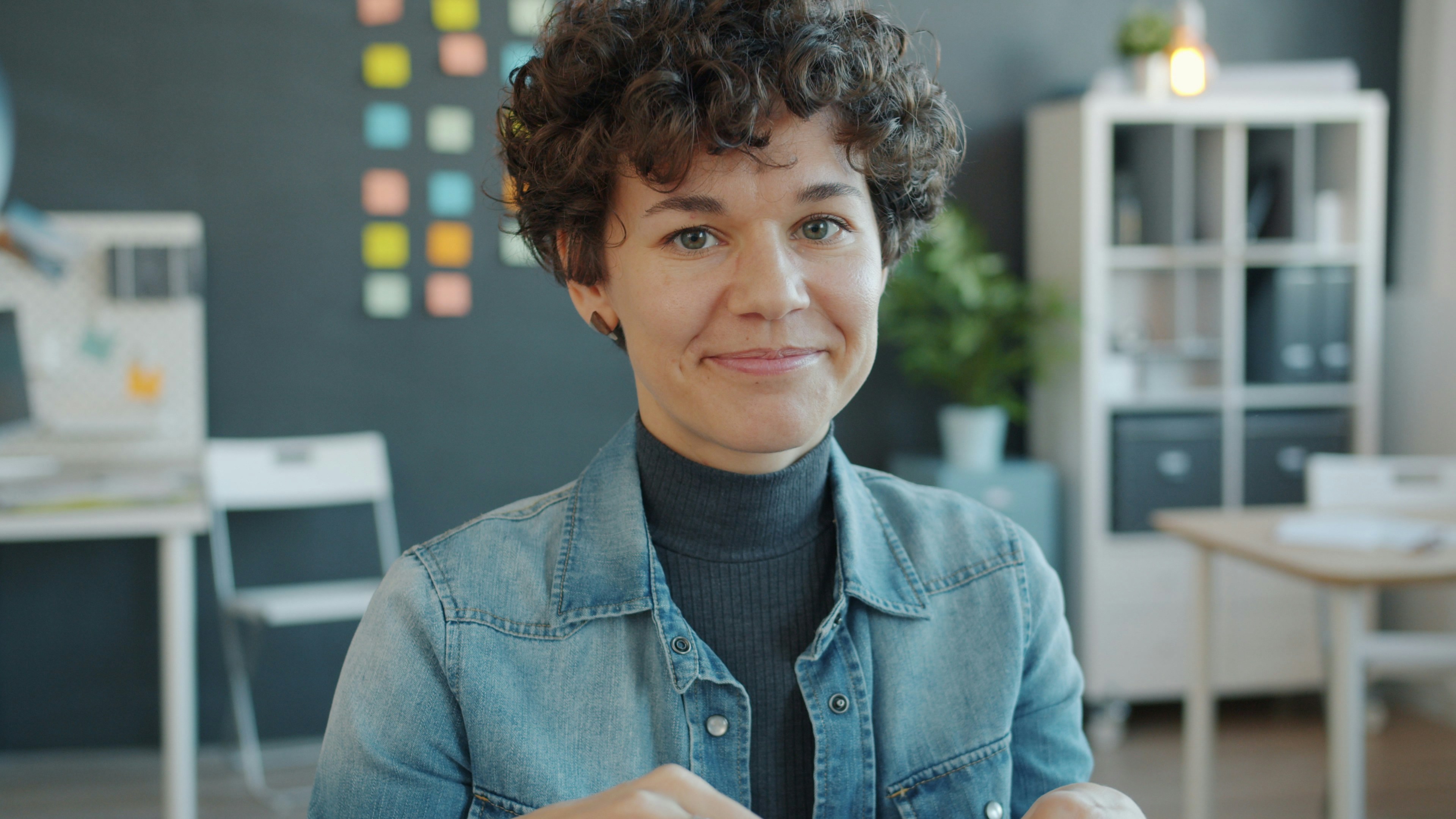 A woman with curly hair smiles in an office.