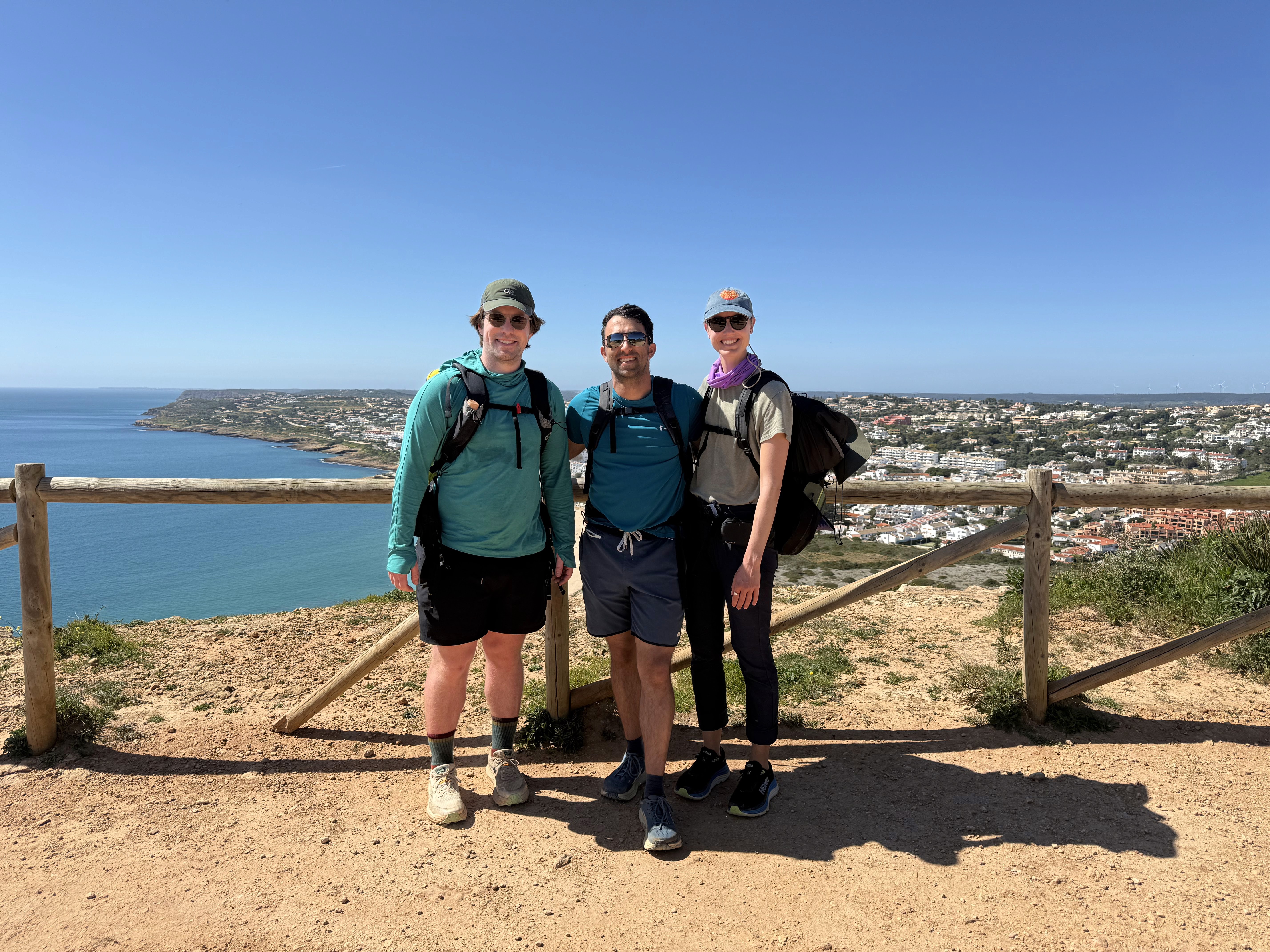 Three people pose in front of a view of the ocean on a sunny day.