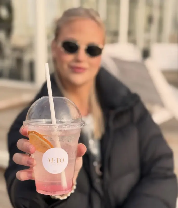 Asiakas pitelee Aeto Gardenin pinkkiä Craft Lemonade -juomaa AETO-mukissa