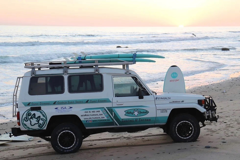 Branded surf safari van parked on a beach at sunset.