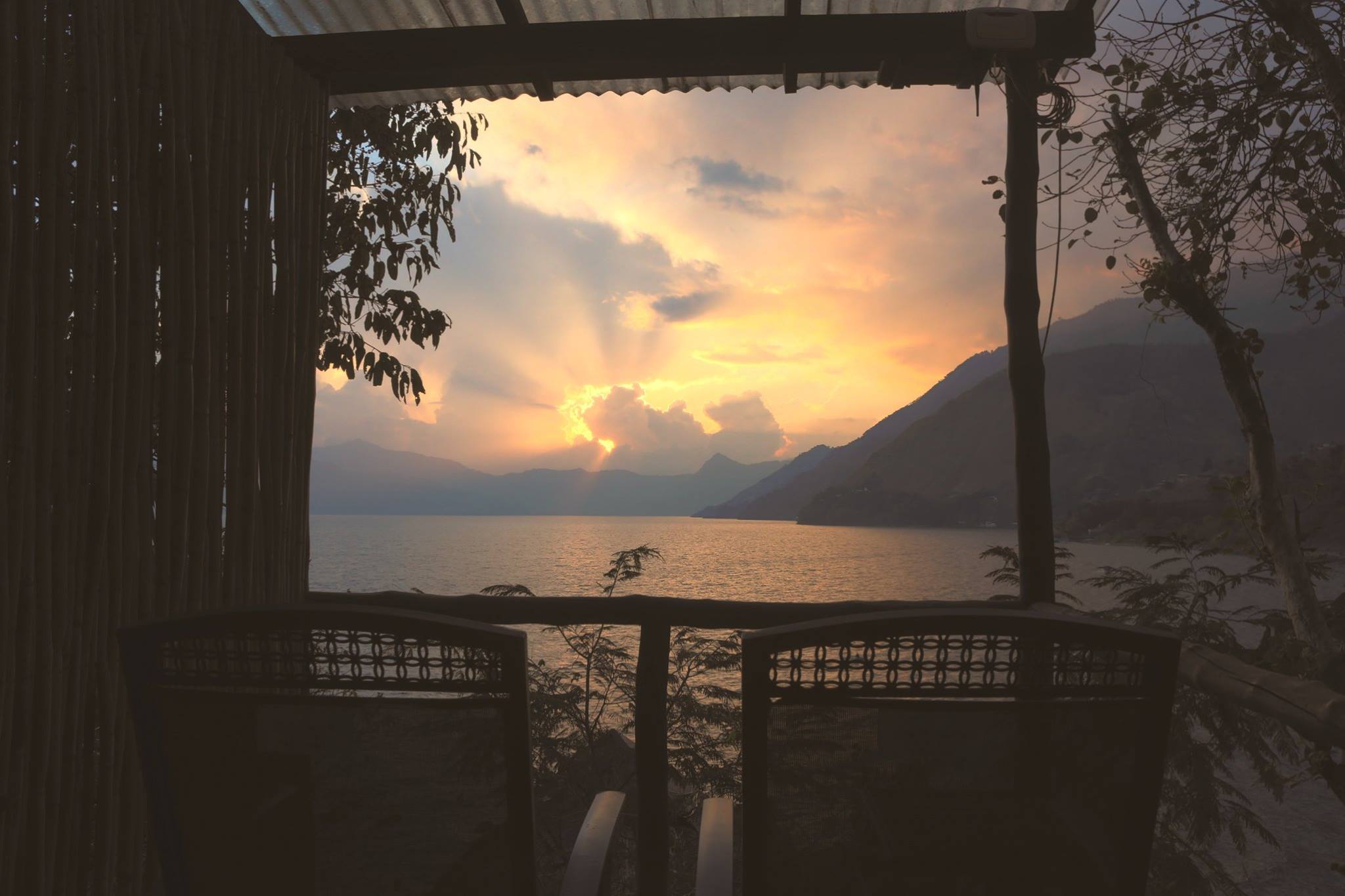 Orange sunset behind clouds, from a wooden balcony overlooking Lake Atitlan