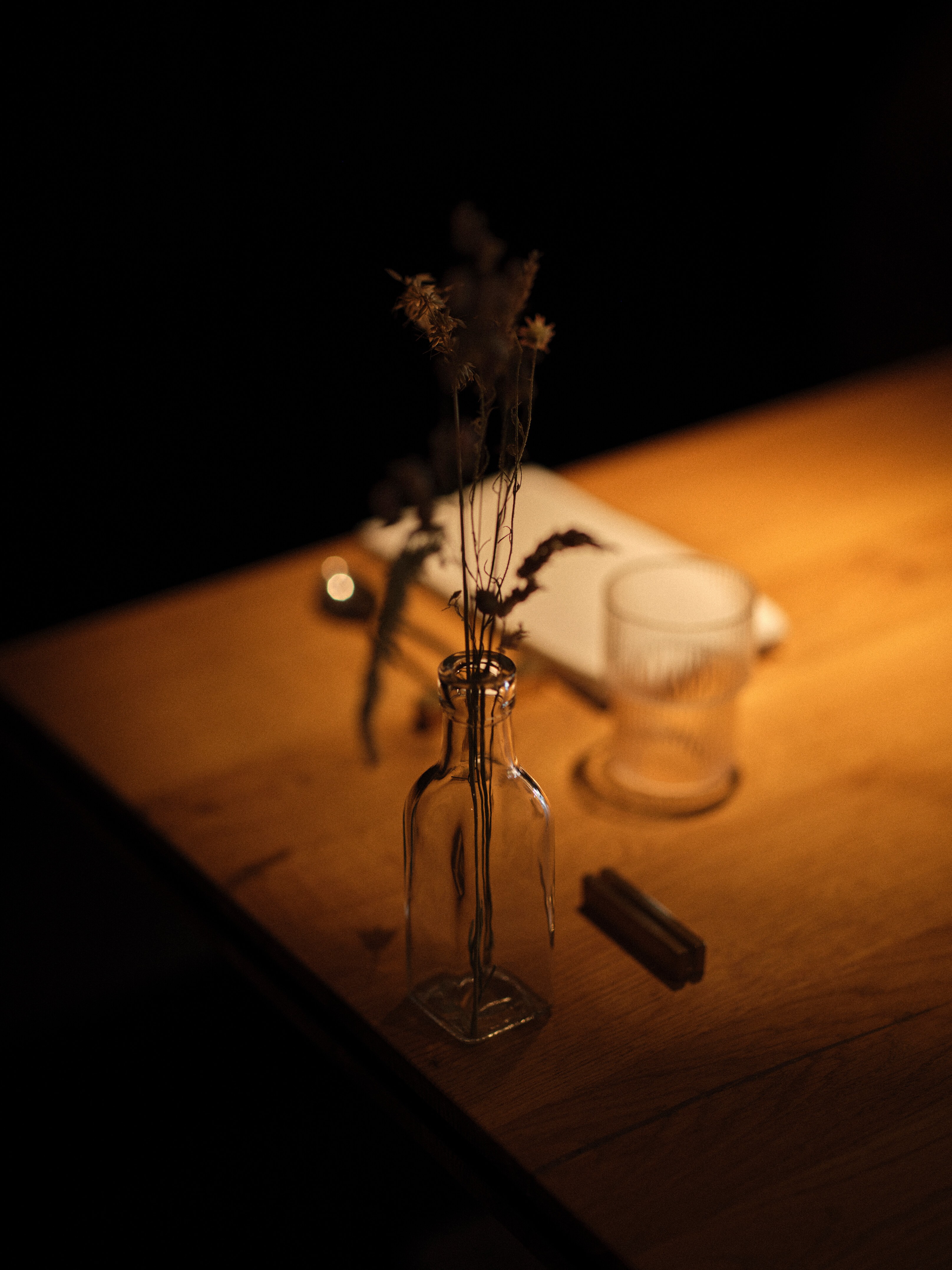 Dining area with set wooden tables, candles, and a long, colorful mural; view towards the kitchen.