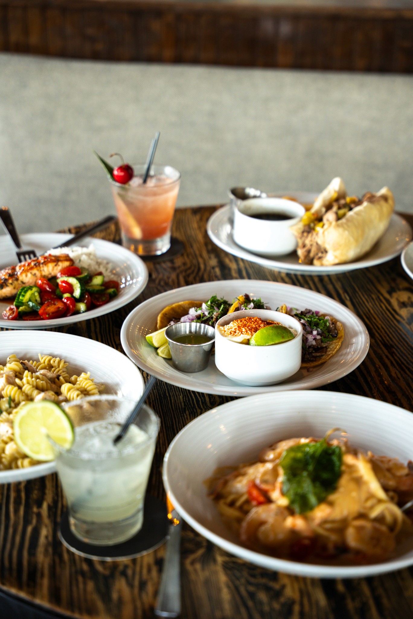 A smiling couple takes a selfie under a clear blue sky. The woman wears a red jacket, and the man, in a green top, holds a smartphone.