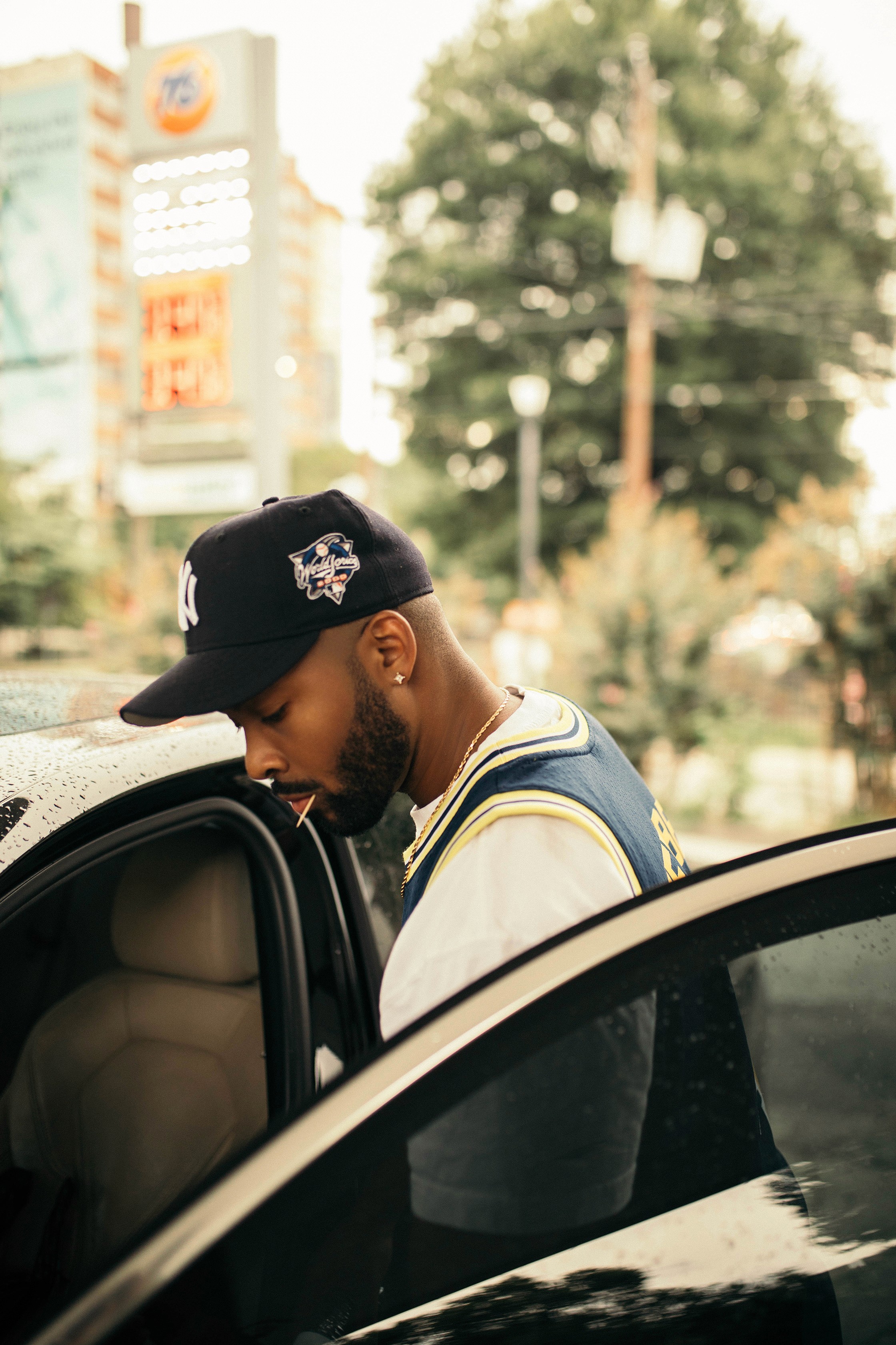 Hollywood Cole, music producer, stands by a car wearing a Yankees cap, sharing insights on collaborations with Jack Harlow and JID in a Studio Talks interview.