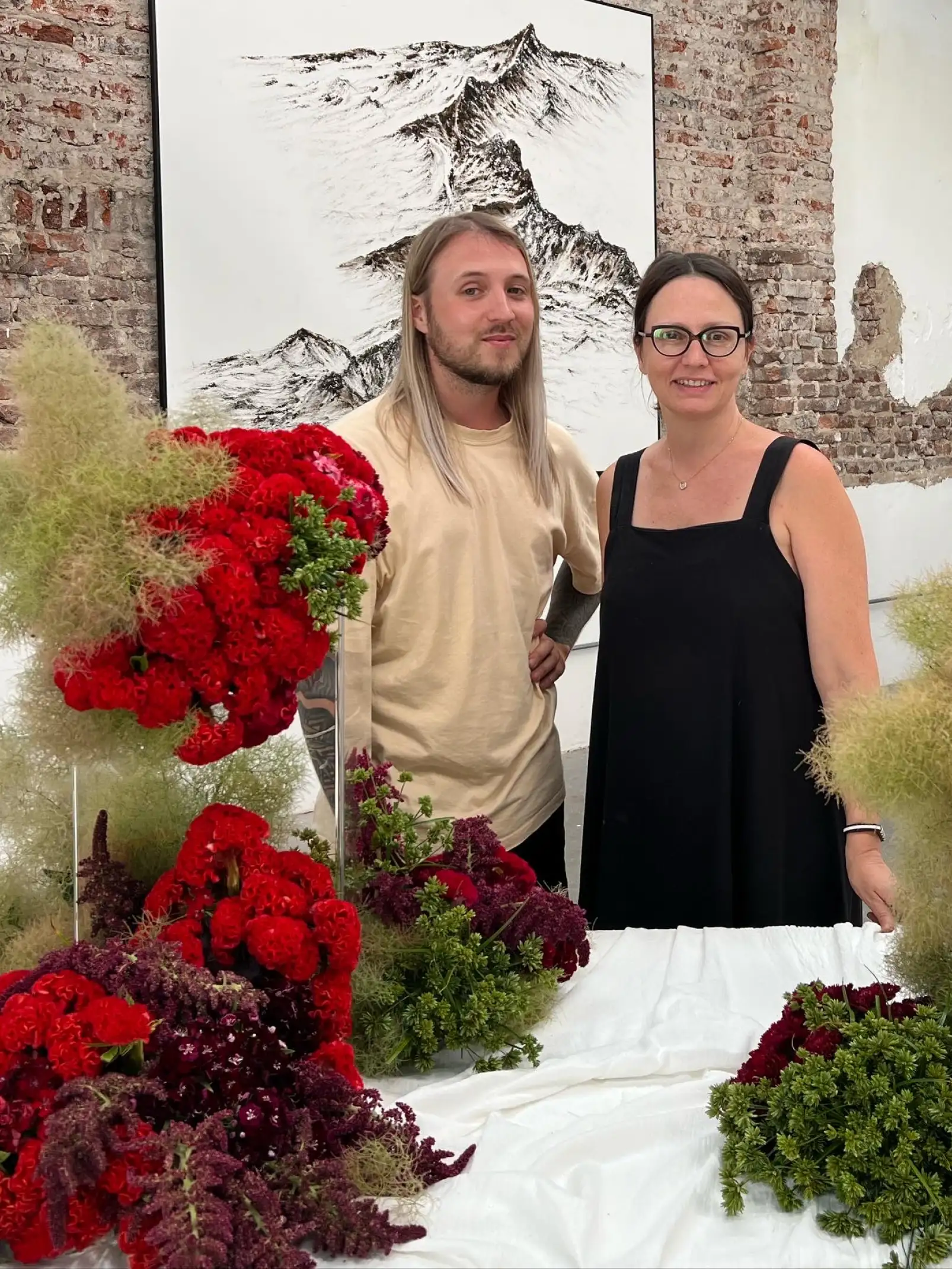 Retrato en galería con instalación floral y la artista Irina Khatsernova junto a colaborador, para prensa y curadores que documentan proyectos de arte contemporáneo con enfoque botánico.