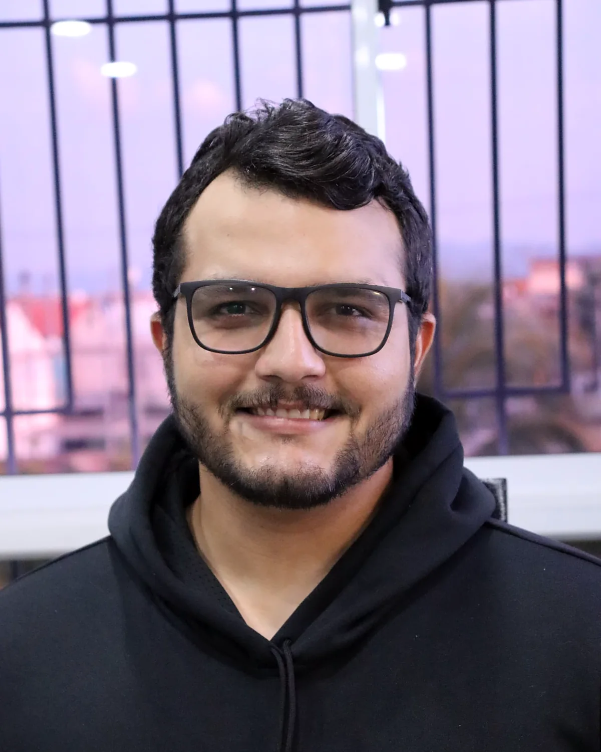 Portrait of Alejandro Vasquez smiling, wearing glasses and a black hoodie