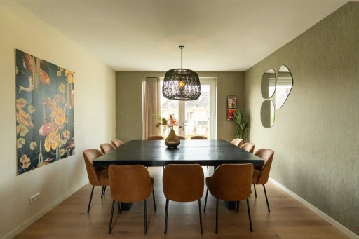 De eethoek met een lange tafel, zes stoelen, ronde spiegels en een kleurrijk schilderij.