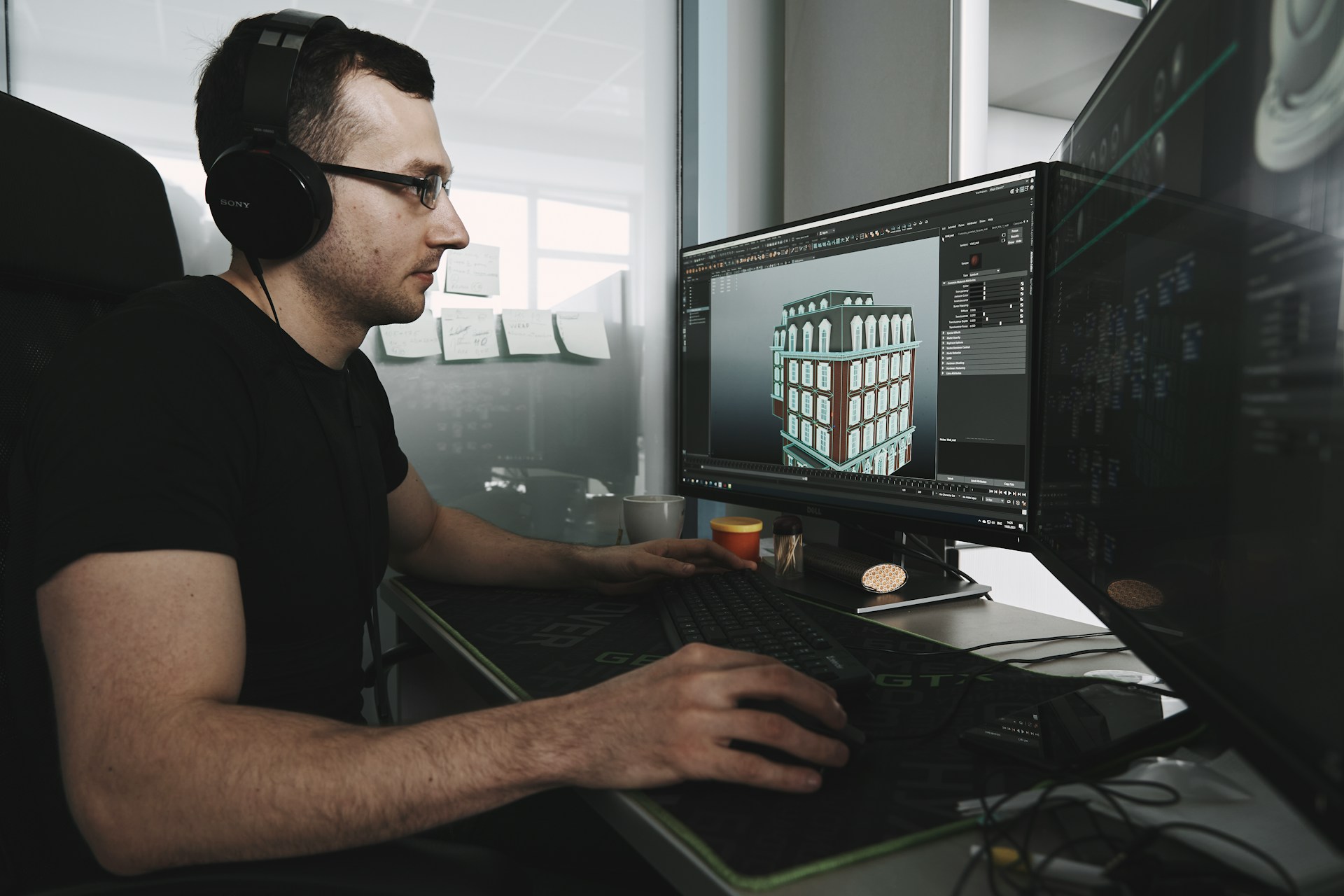 A 3D artist working on a detailed architectural rendering of a building on a dual-monitor setup, showcasing the precision and quality of their 3D product rendering services.