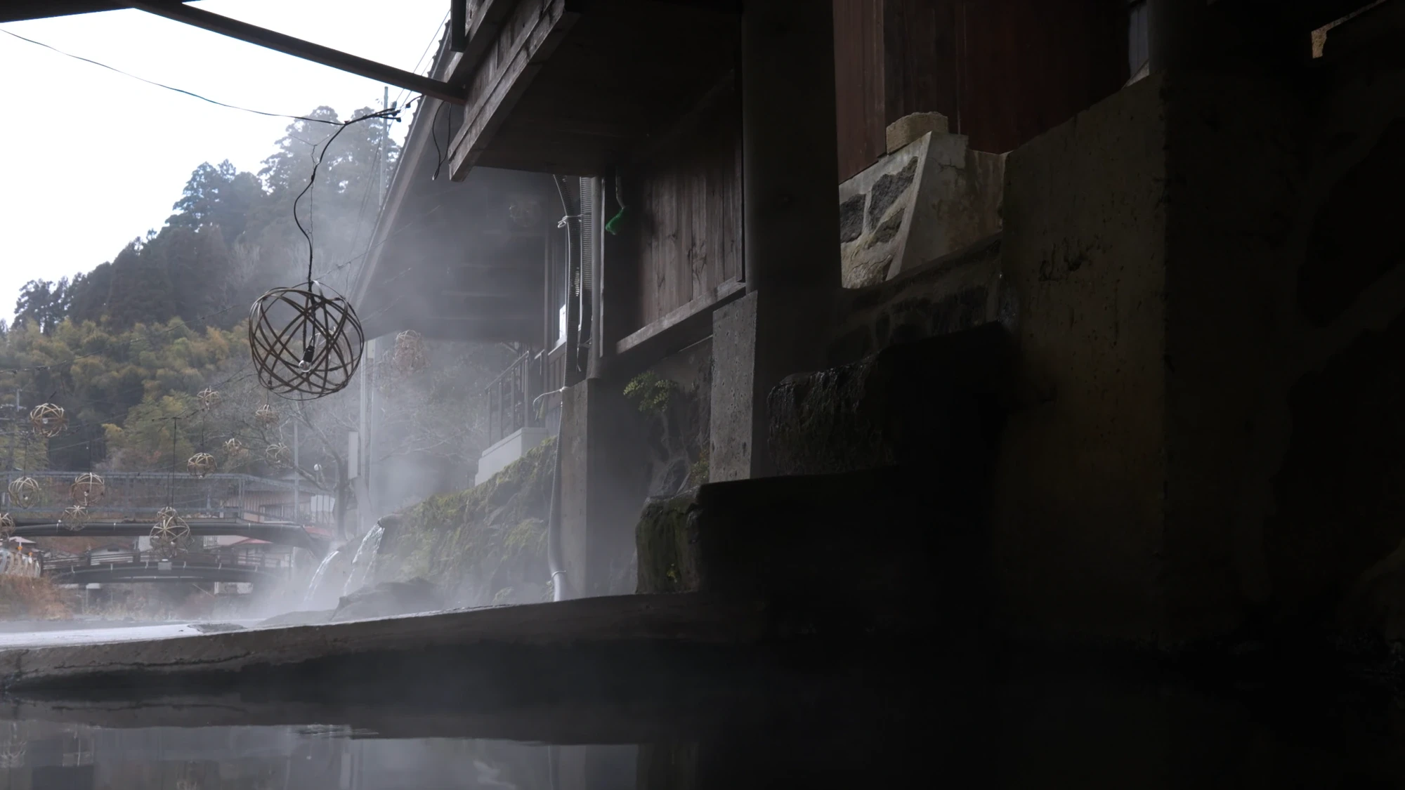 A steaming riverside bath under a timber eave at Kurokawa Onsen