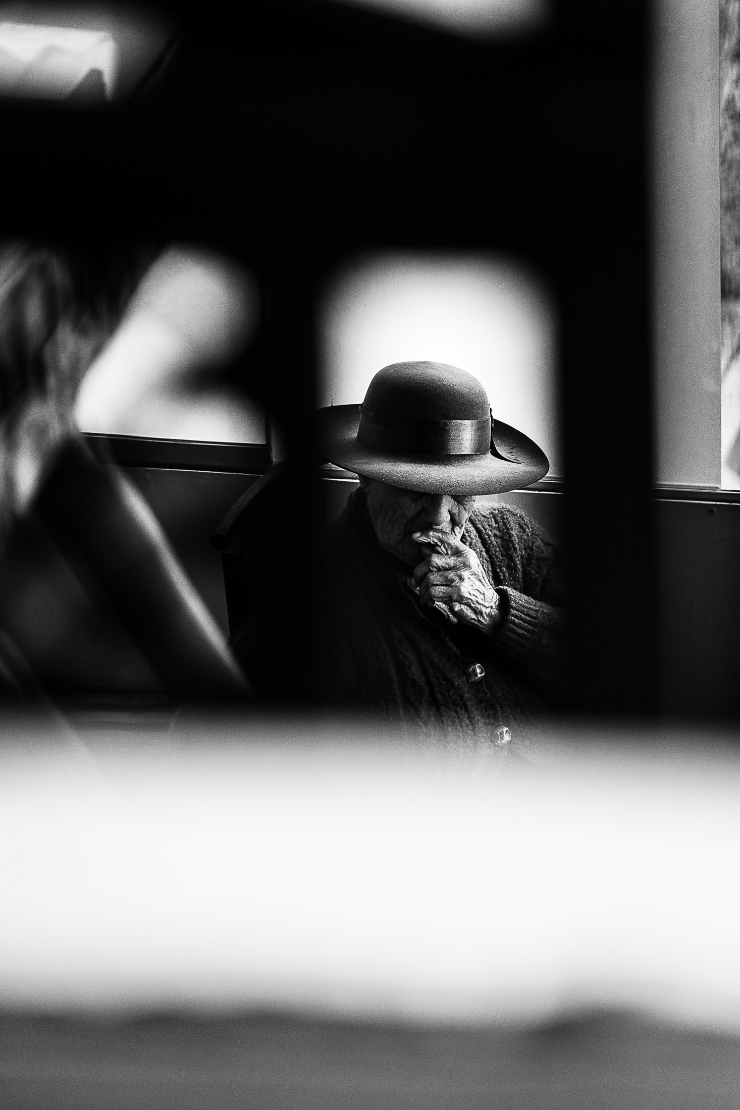 Black and white photograph of elderly woman wearing hat sitting by window inside public transport.