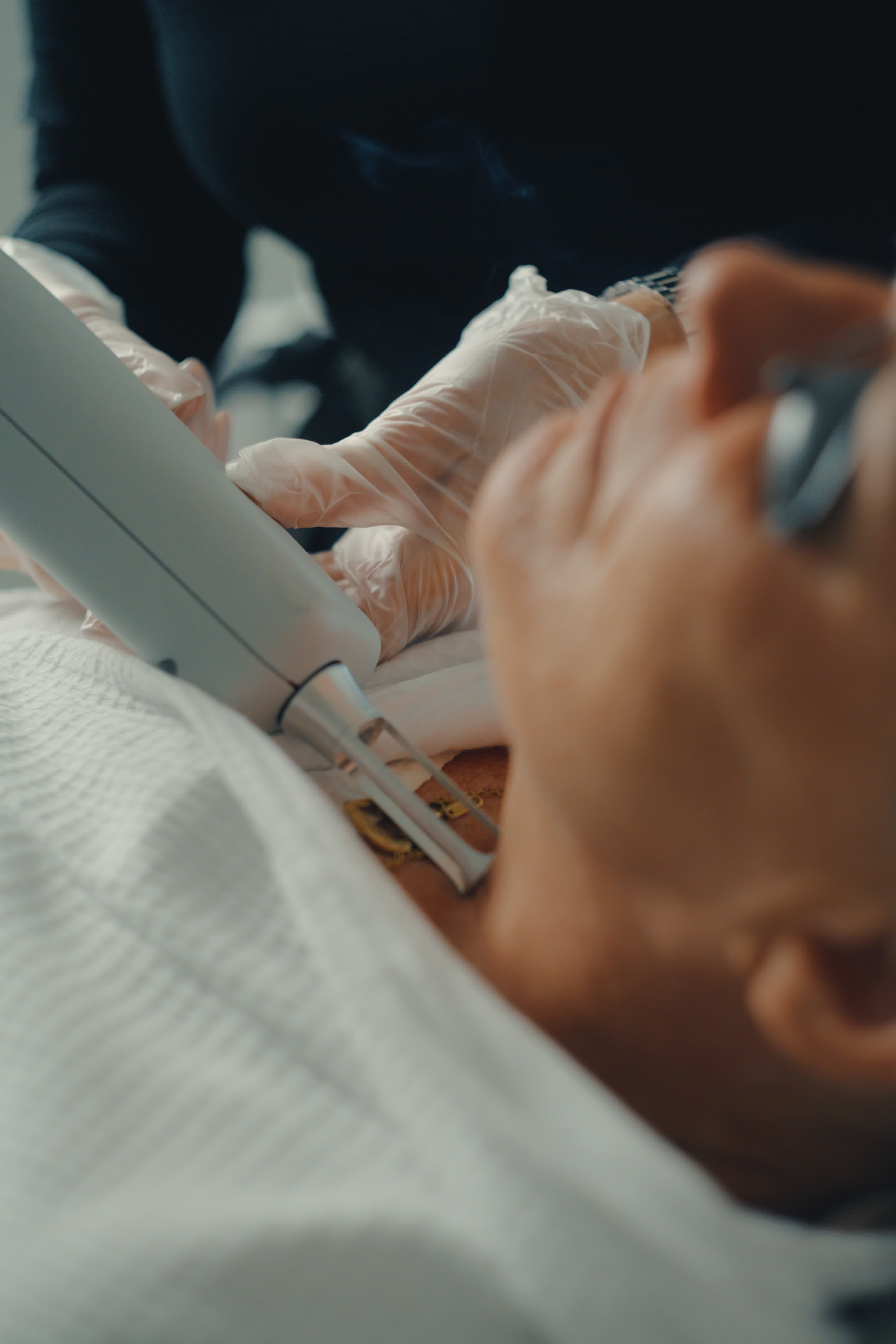 Gloved hands use a facial treatment device on a person's neck.