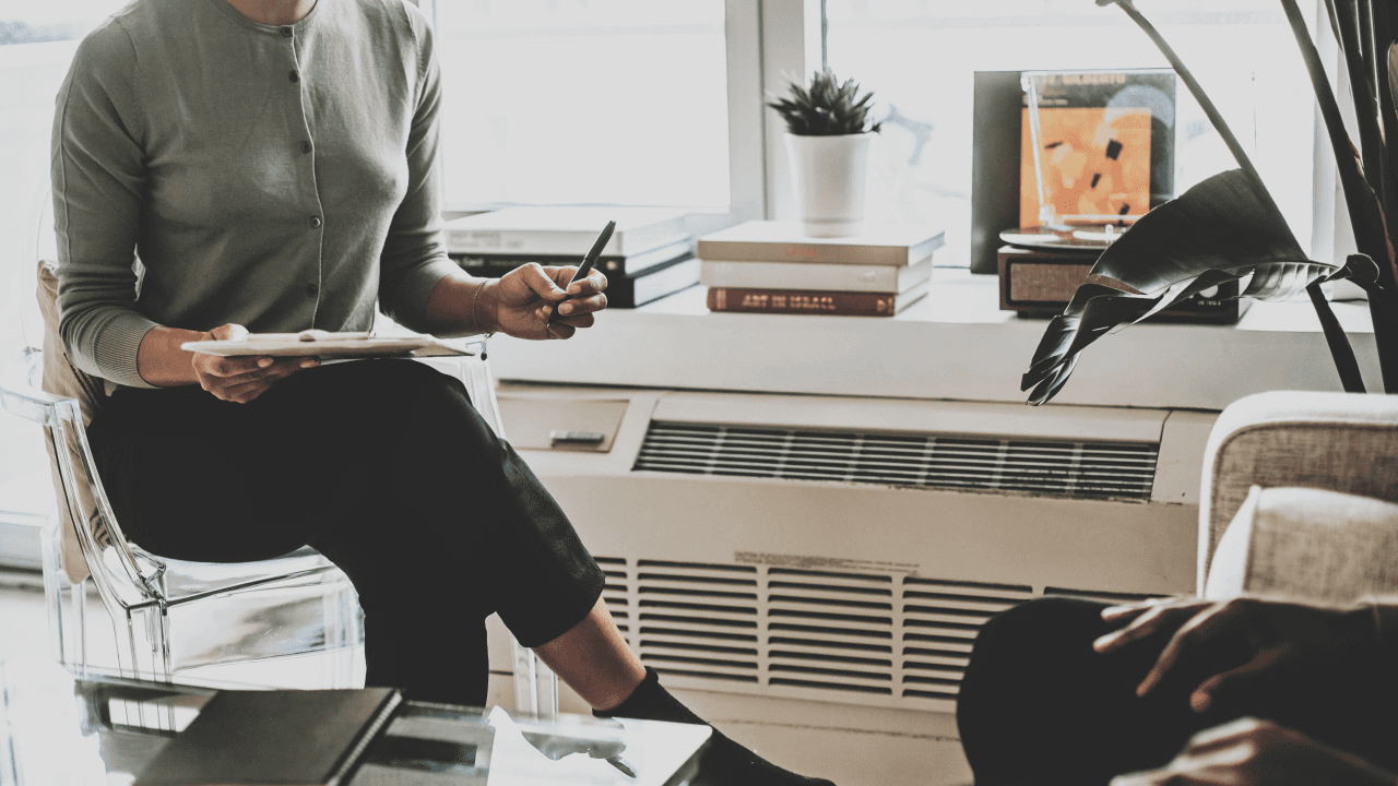 An interviewer with a clipboard listening to a candidate across an office desk