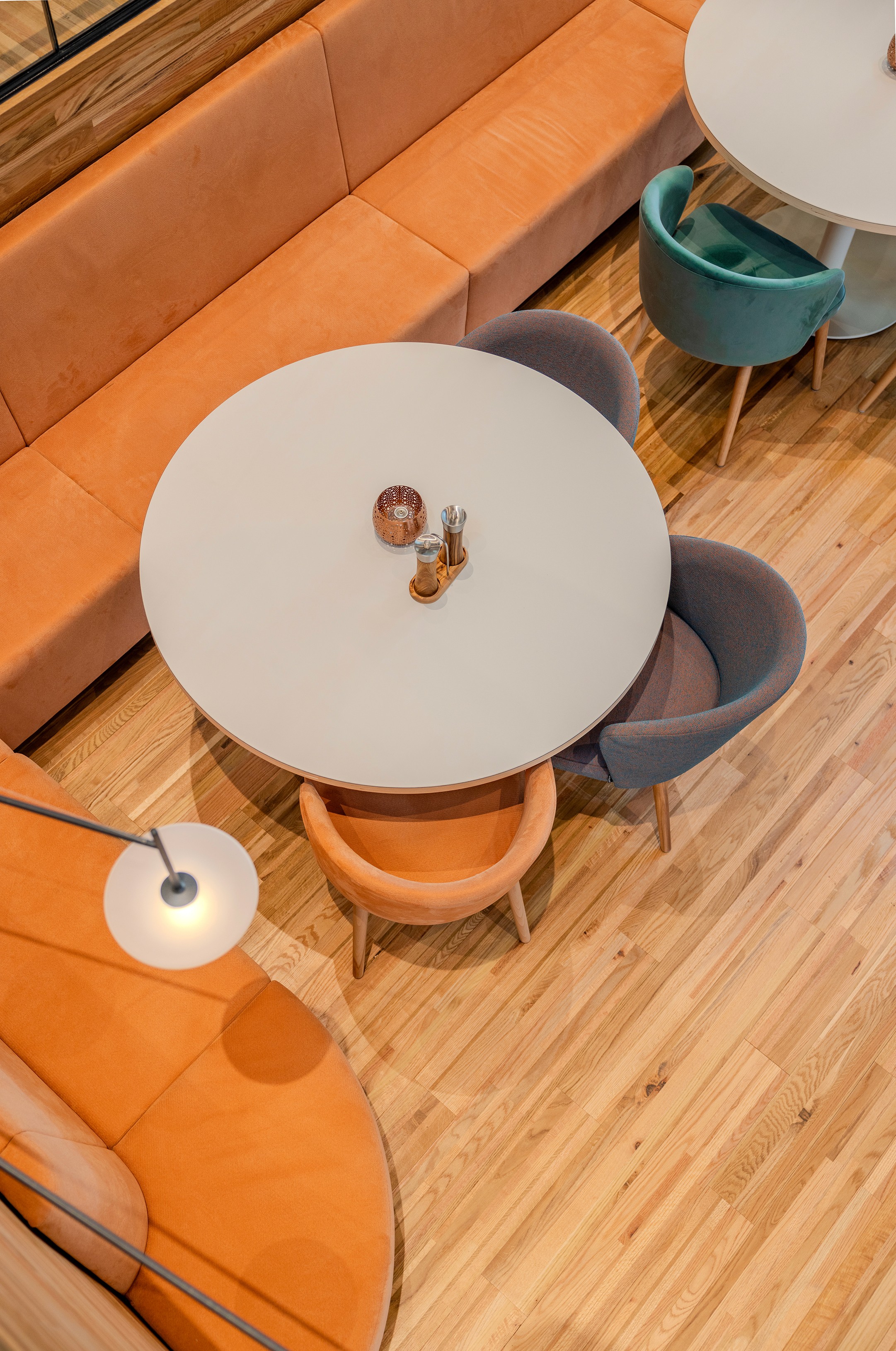 Bovenaanzicht van een informele zithoek in AFAS DotNL met een ronde witte tafel, oranje en grijze banken en een vloerlamp op een warme houten vloer